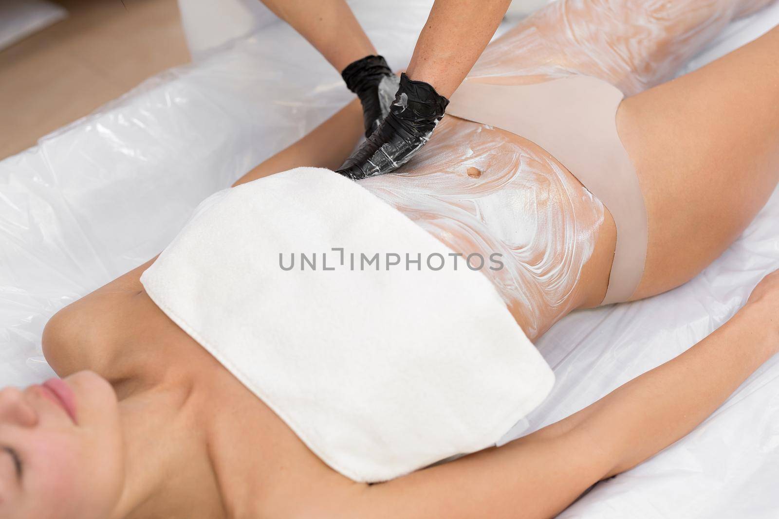 Cosmetologist applies a moisturizing mask on the body of a young girl in a cosmetology clinic before the wrapping procedure. Body Care. Spa Treatment.