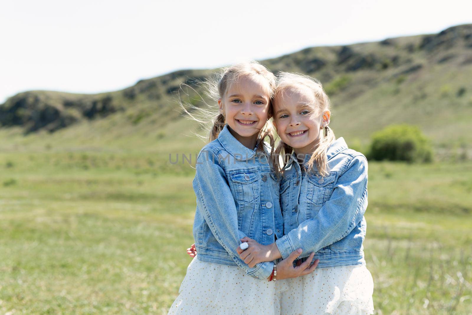 Portrait of two twin sisters who embrace in a meadow in nature.