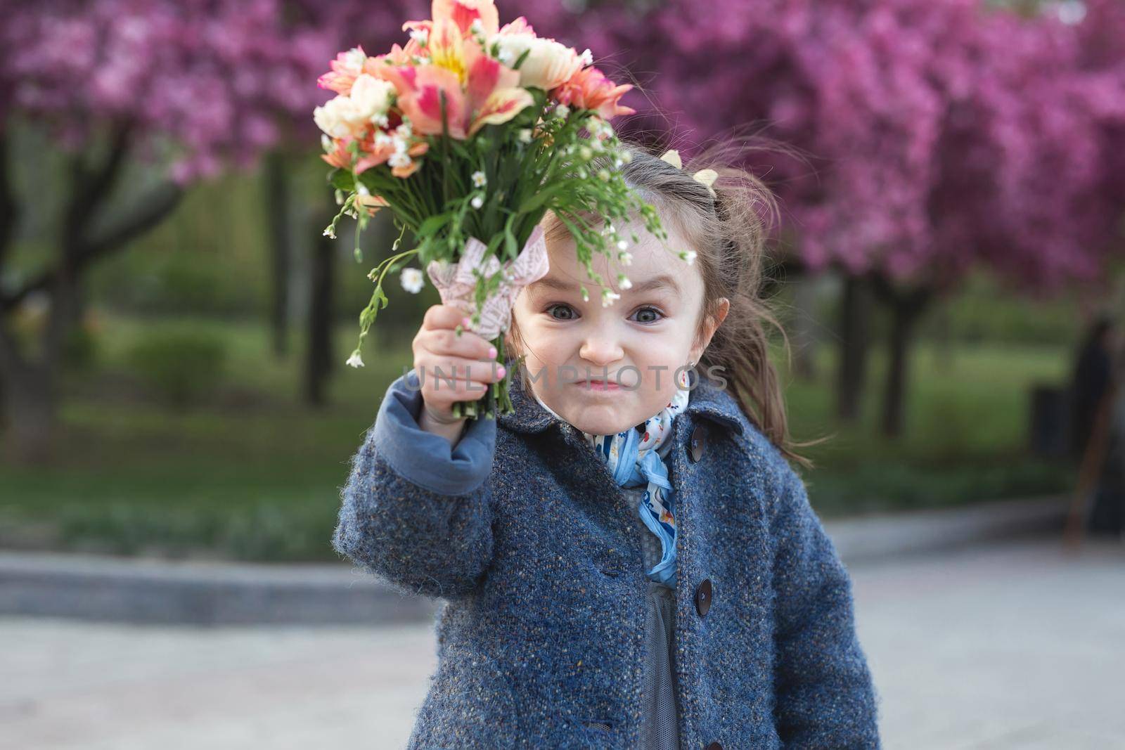 Little girl in a park in the spring is threatening the camera and waving a bouquet of flowers.