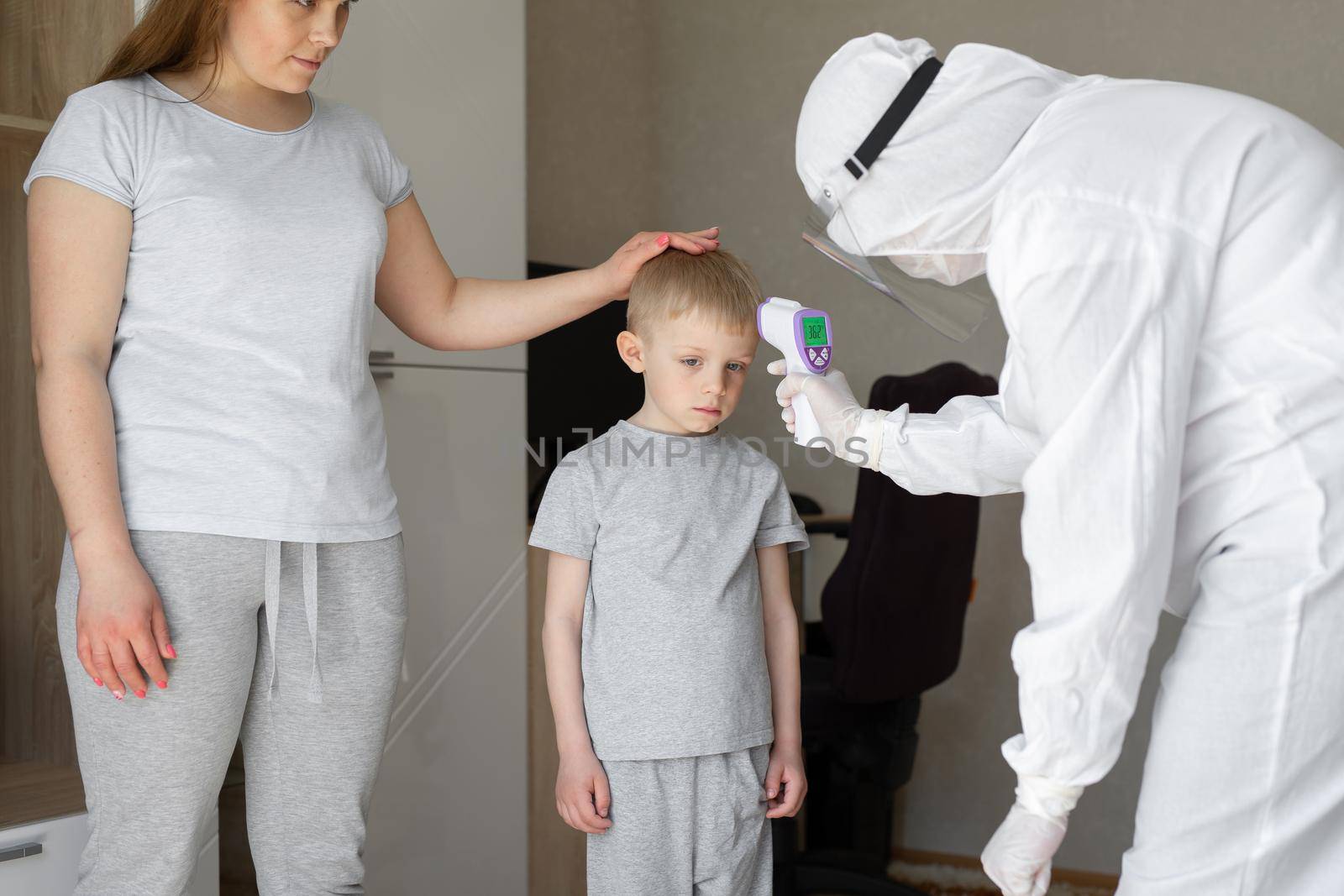 Pediatrician or doctor checks elementary age boy's body temperature using infrared forehead thermometer gun for virus symptom - epidemic coronavirus outbreak concept.