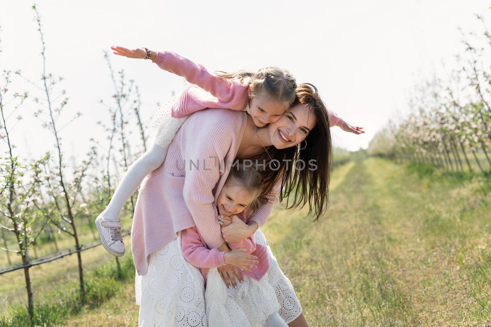 Happy family in the Apple orchard. Mom and two twin daughters have fun and hug.