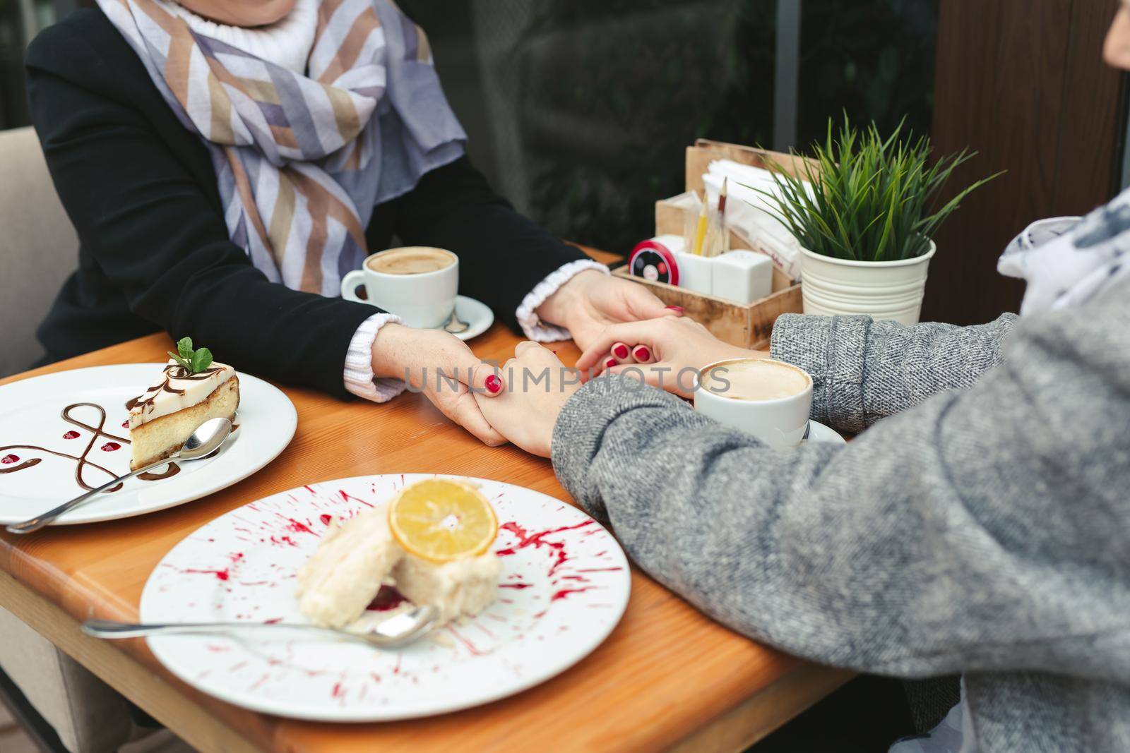 Close-up of a mother and daughter's hands on a wooden table in a cafe. Adult mother and daughter hold hands and drink coffee.