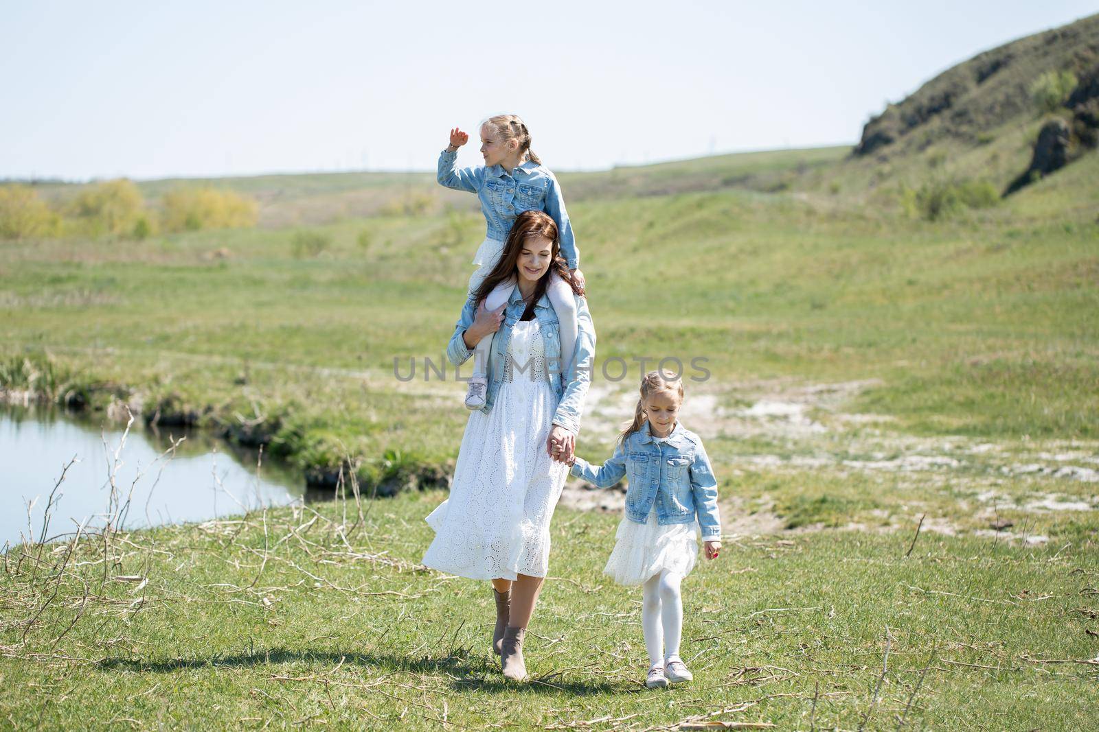 Mother and her twin daughters walk along a path near a reservoir in the village by StudioPeace