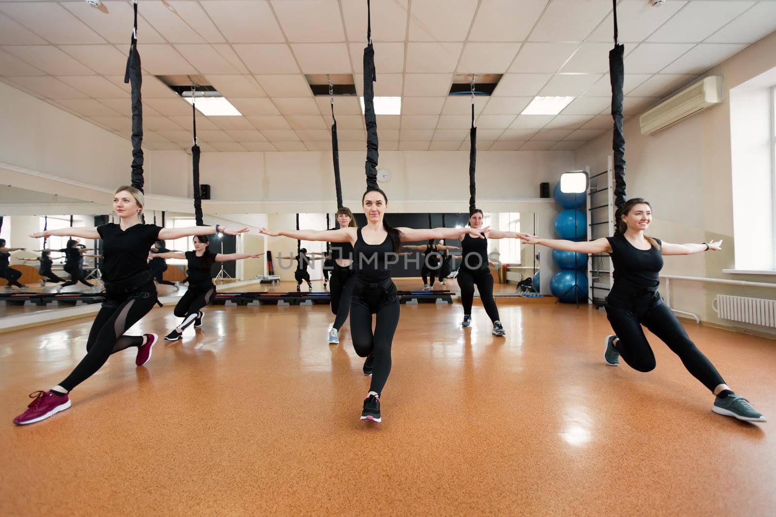 Group of active sports girls in black sportswear are engaged in budgie fitness in the gym. Bungee jumping in the gym. by StudioPeace