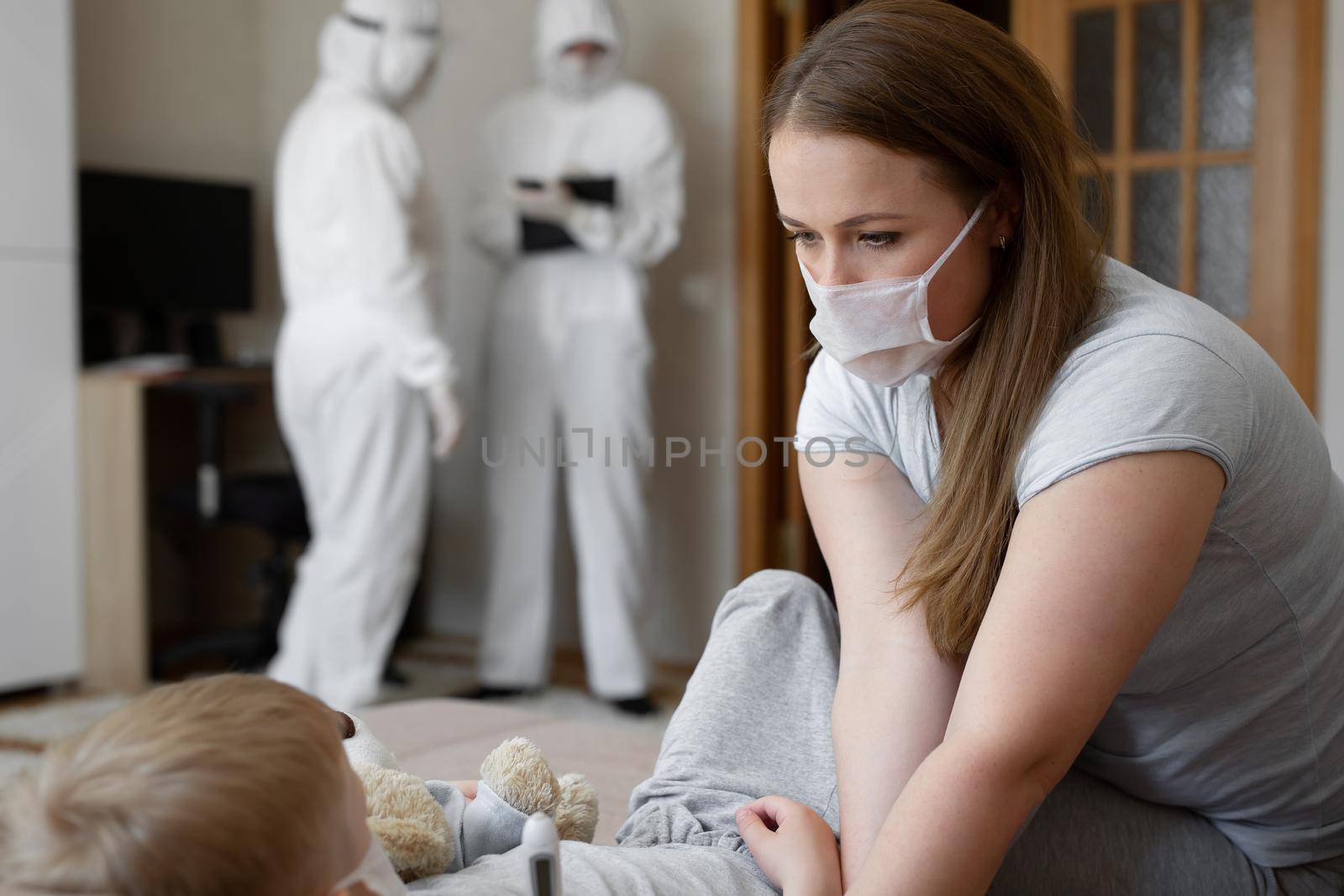 Mom measures baby's temperature. Doctors in protective suits at sick patients at home. Coronavirus, covid-19 by StudioPeace