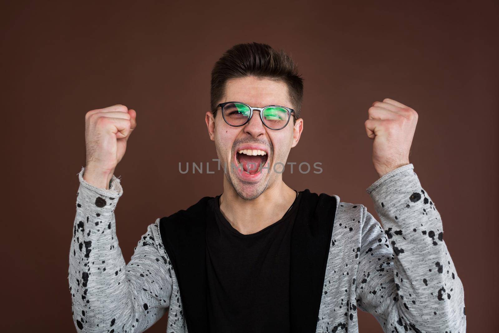 Happy positive excited young man clenching fists and screaming, wearing casual t-shirt glad to hear good news, celebrating his victory or success. Life achievement, goals and happiness concept.
