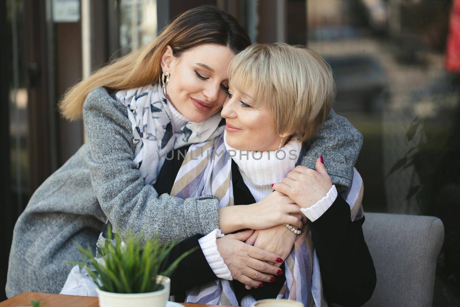 An adult daughter hugs and kisses her elderly mother when they meet in a cafe.
