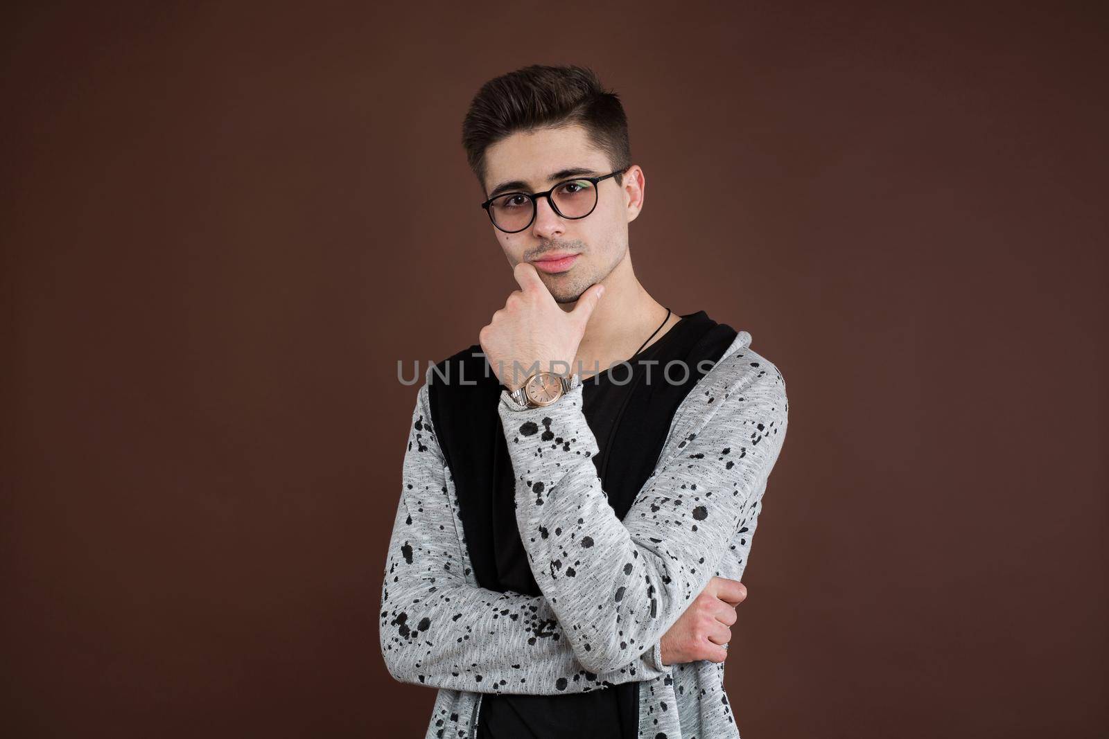 Young man in depression. Stylish male student wears round spectacles, has trendy hairstyle, looks confidently, isolated over brown background. People and human expressions. by StudioPeace