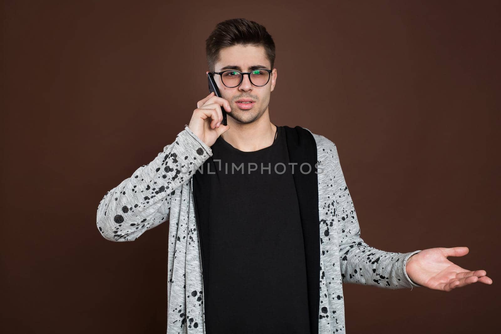 Attractive man standing on brown isolated background and talking per mobile phone.