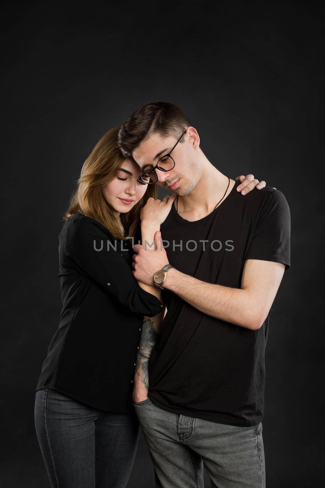 Portrait of young couple in black clothes wearing trendy glasses and posing over black background.