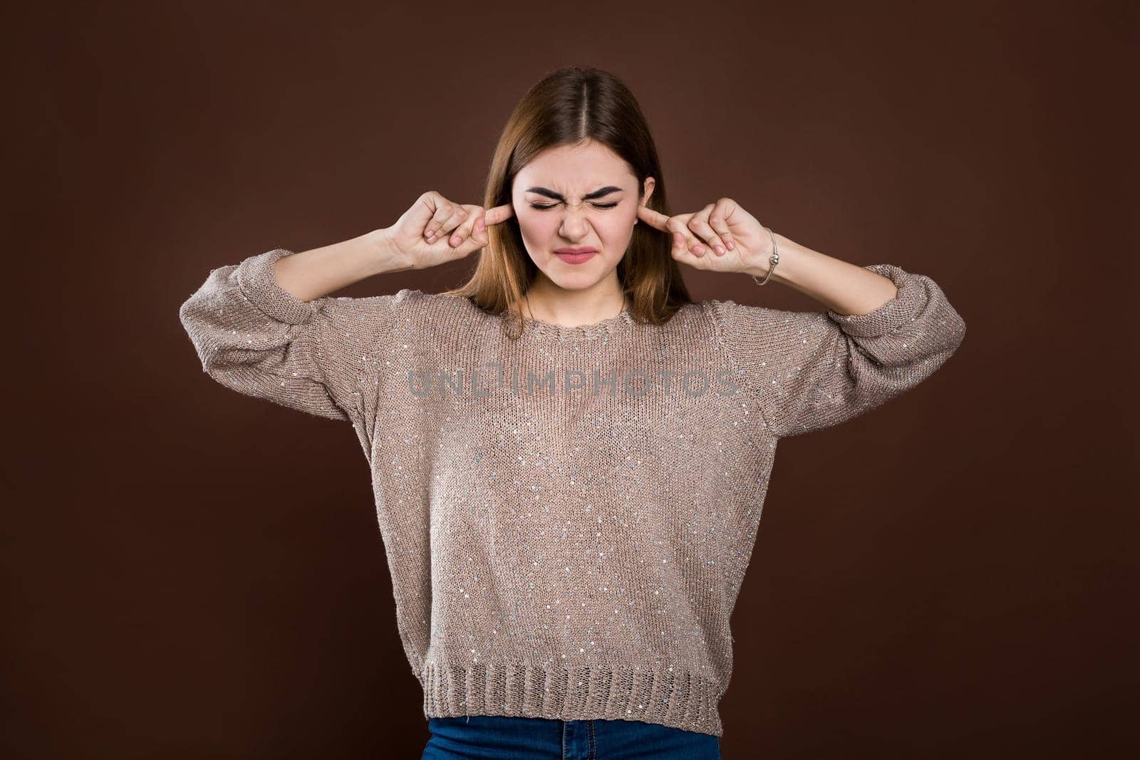 Close up portrait of angry stressed out young woman plugging ears with fingers, irritated with loud annoying noise, having headache or migraine. Negative human emotions