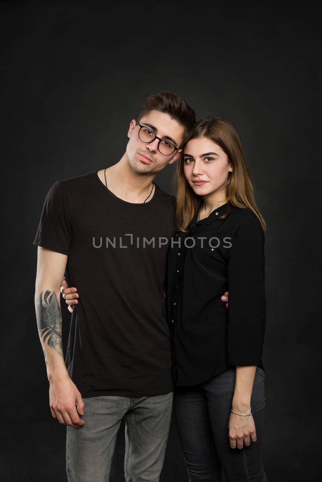 Portrait of young couple in black clothes wearing trendy glasses and posing over black background by StudioPeace