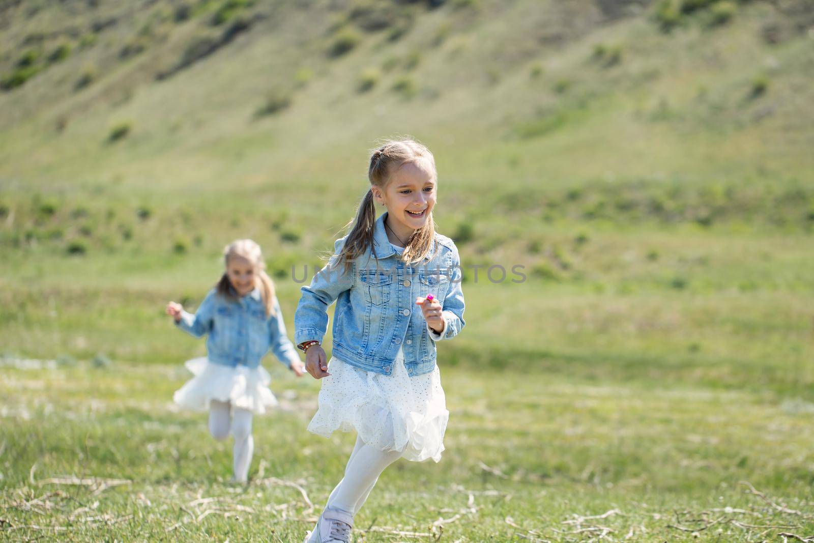 Two little twin sisters run and spin in the meadow.