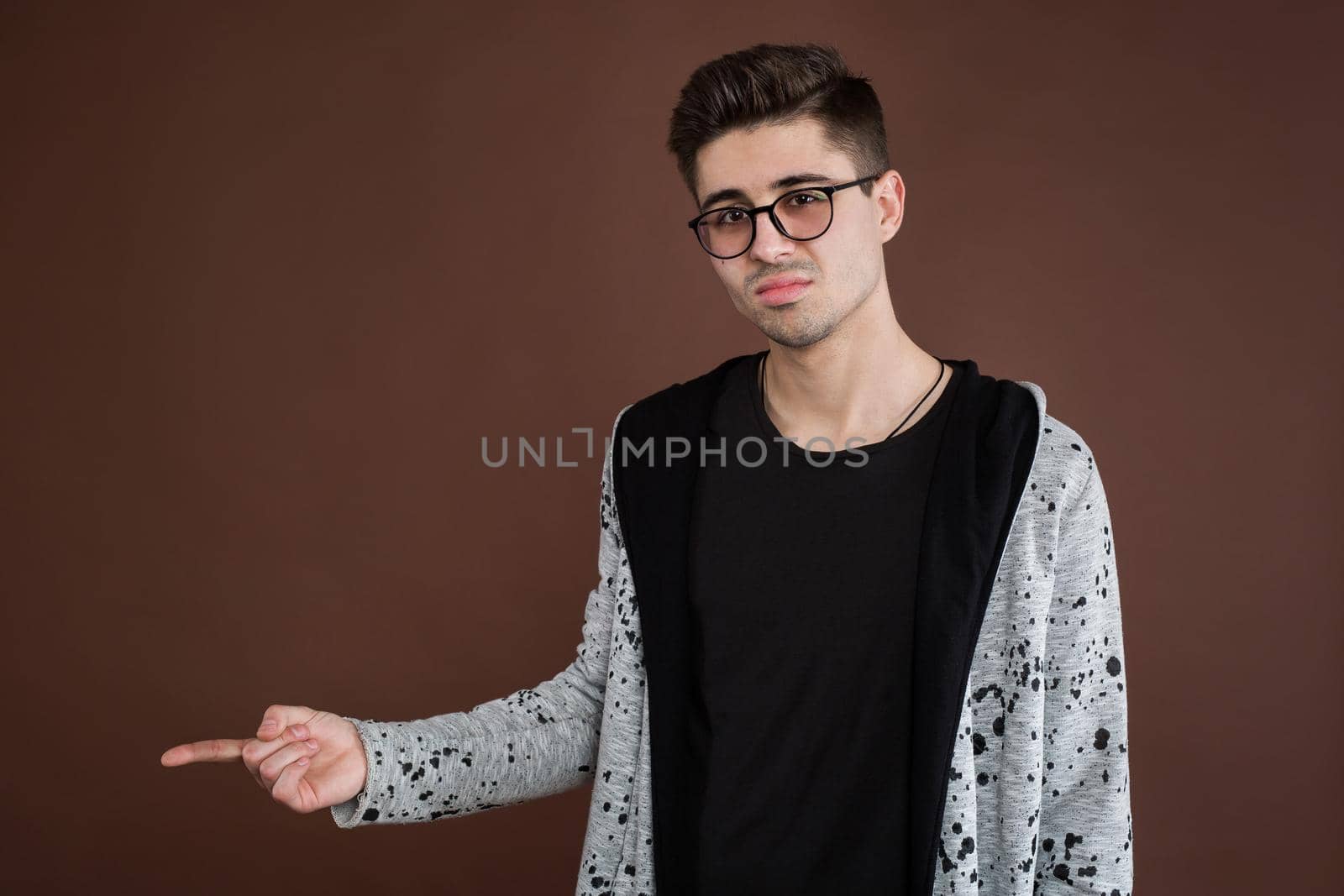 Handsome young adult man in shirt looking at camera and pointing away while standing isolated on brown background. by StudioPeace