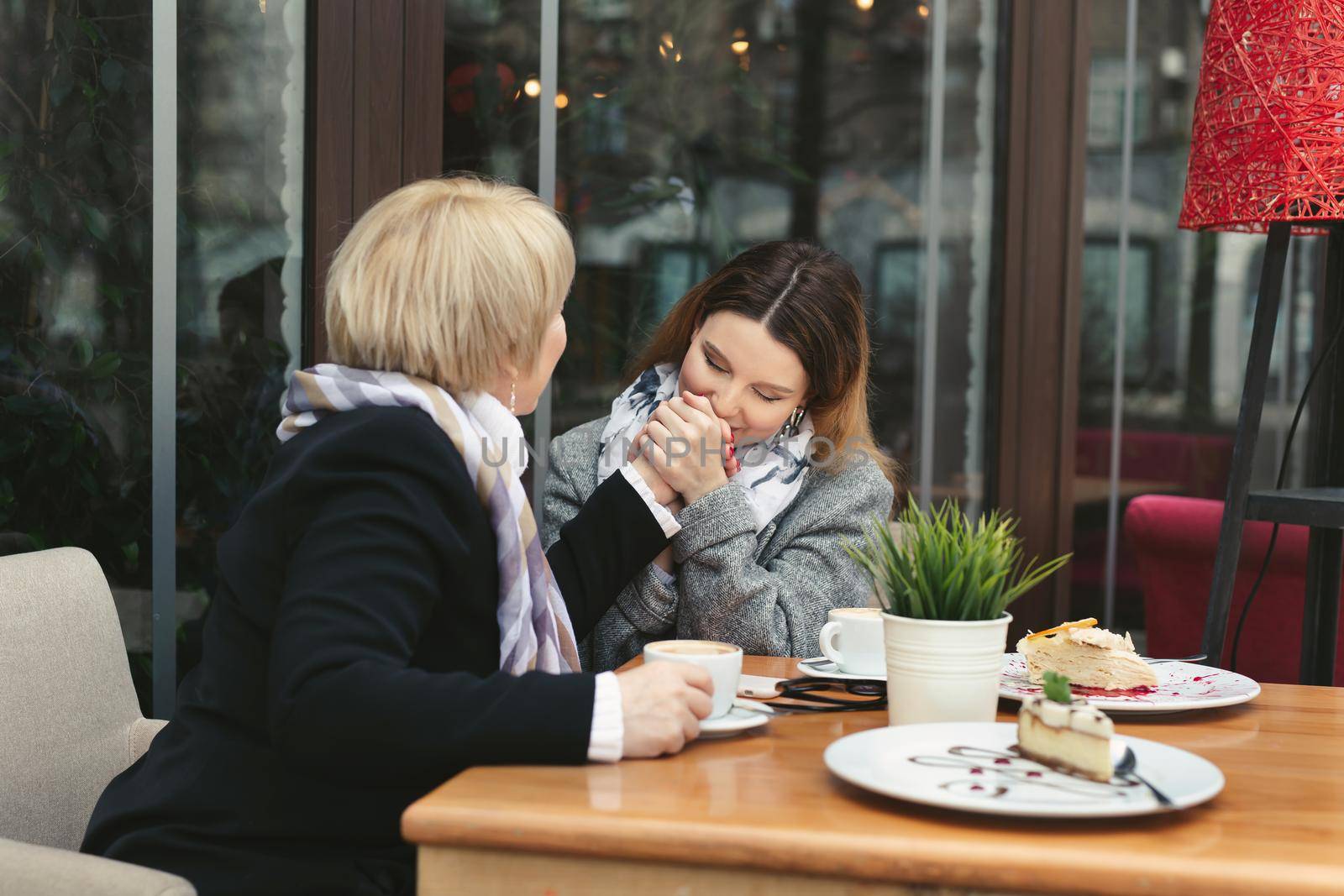 An adult daughter kisses her mother's hand and smiles. Emotions of relatives in the cafe.