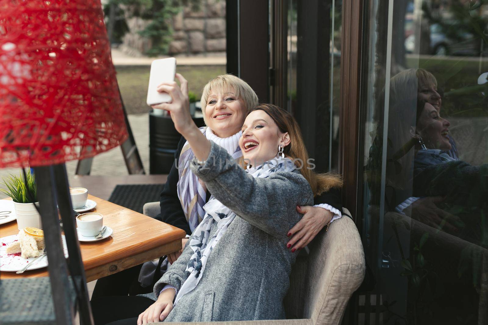 Family and technology. Aged woman and her adult daughter taking selfie on smartphone at sidewalk cafe by StudioPeace