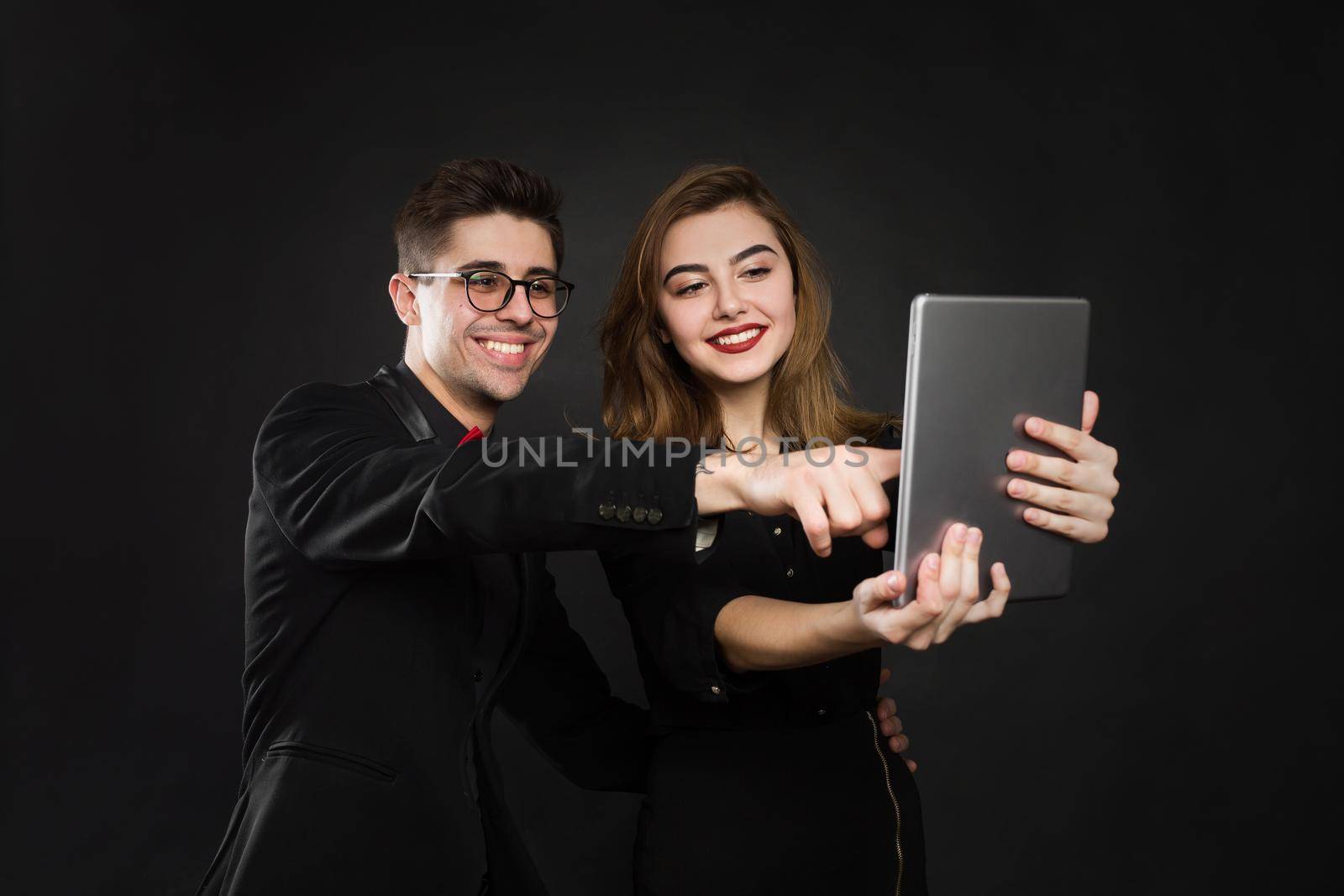 Happy couple pointing finger at digital tablet isolated on black background. by StudioPeace