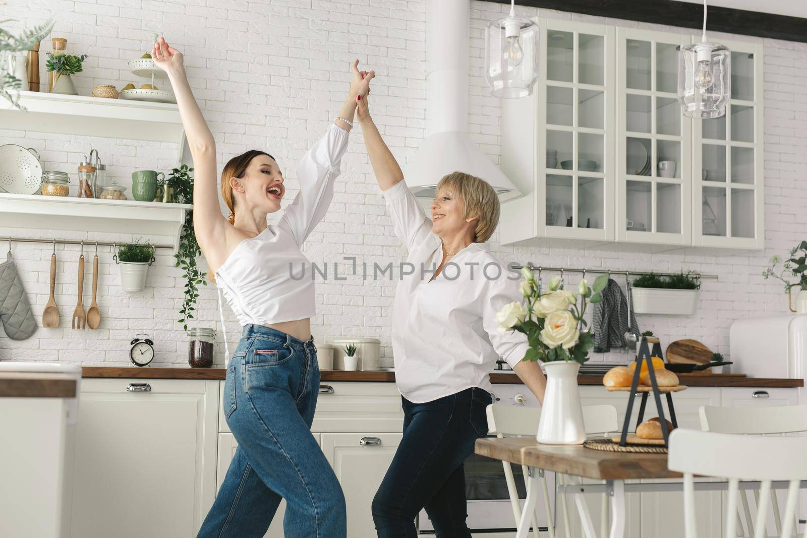 Mother and her adult daughter are having fun and dancing in the kitchen.