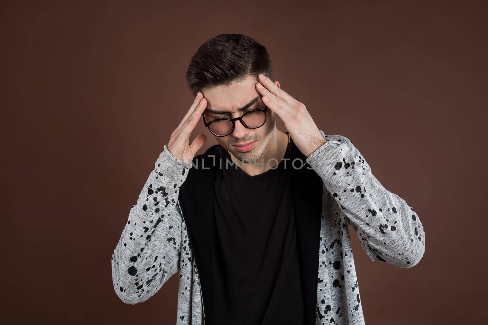 Upset unhappy young man squeezing head with hands, suffering from headache. People, stress, tension and migraine concept