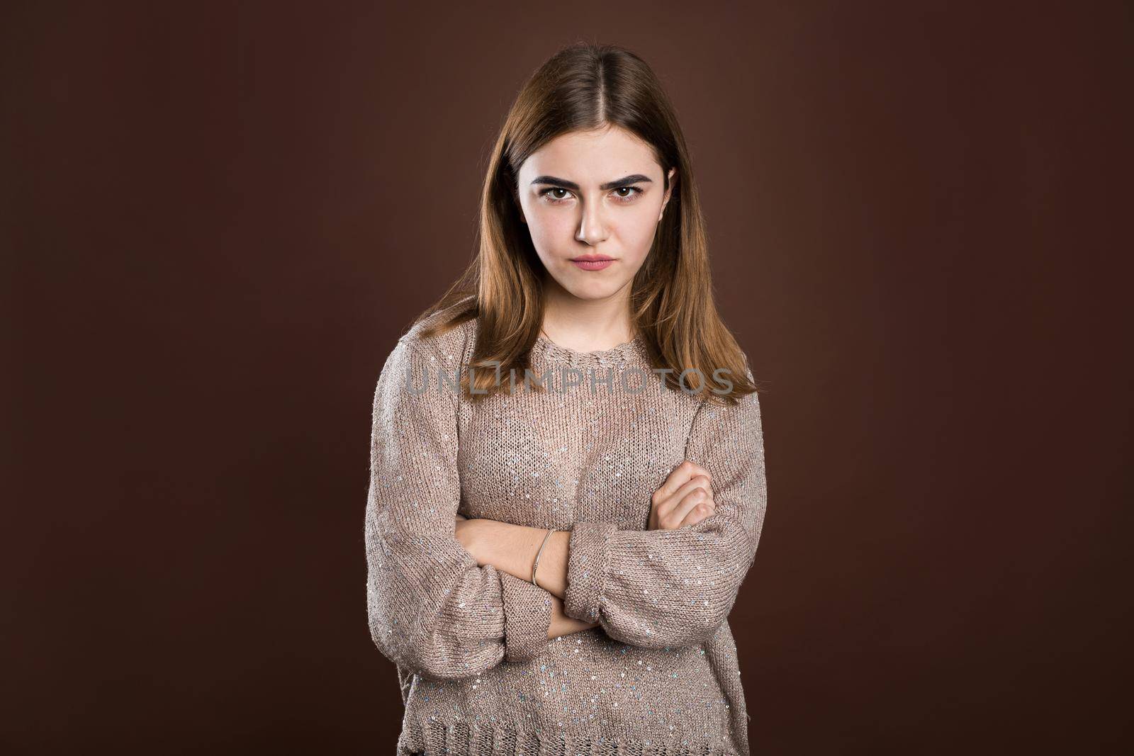 Portrait of beautiful girl frowning her face in displeasure, wearing loose long-sleeved sweater, keeping arms folded. Attractive young woman in closed posture by StudioPeace