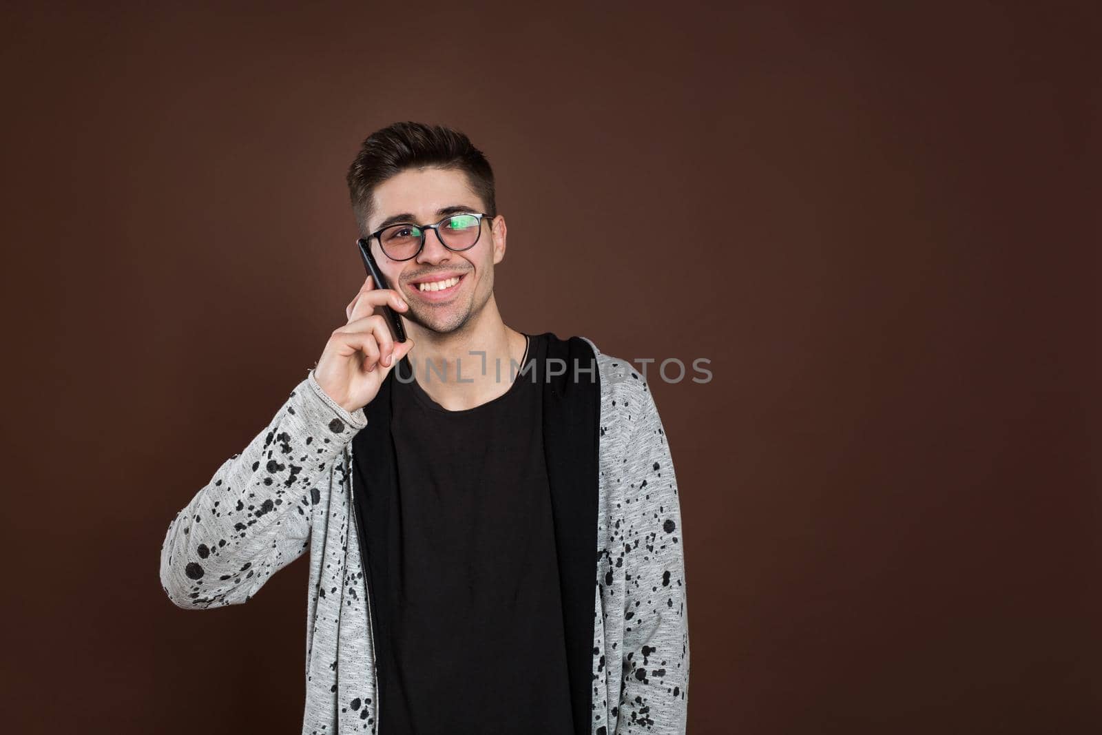 Sweet conversation. Attractive man standing on brown isolated background and talking per mobile phone by StudioPeace