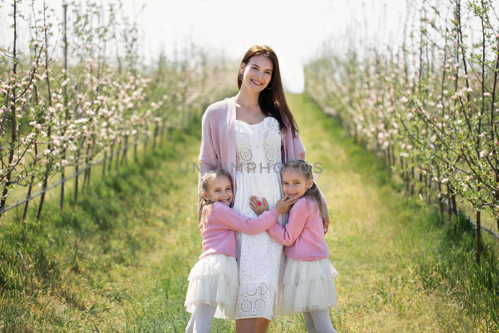 Portrait of a mother and her twin daughters in a blooming Apple orchard.