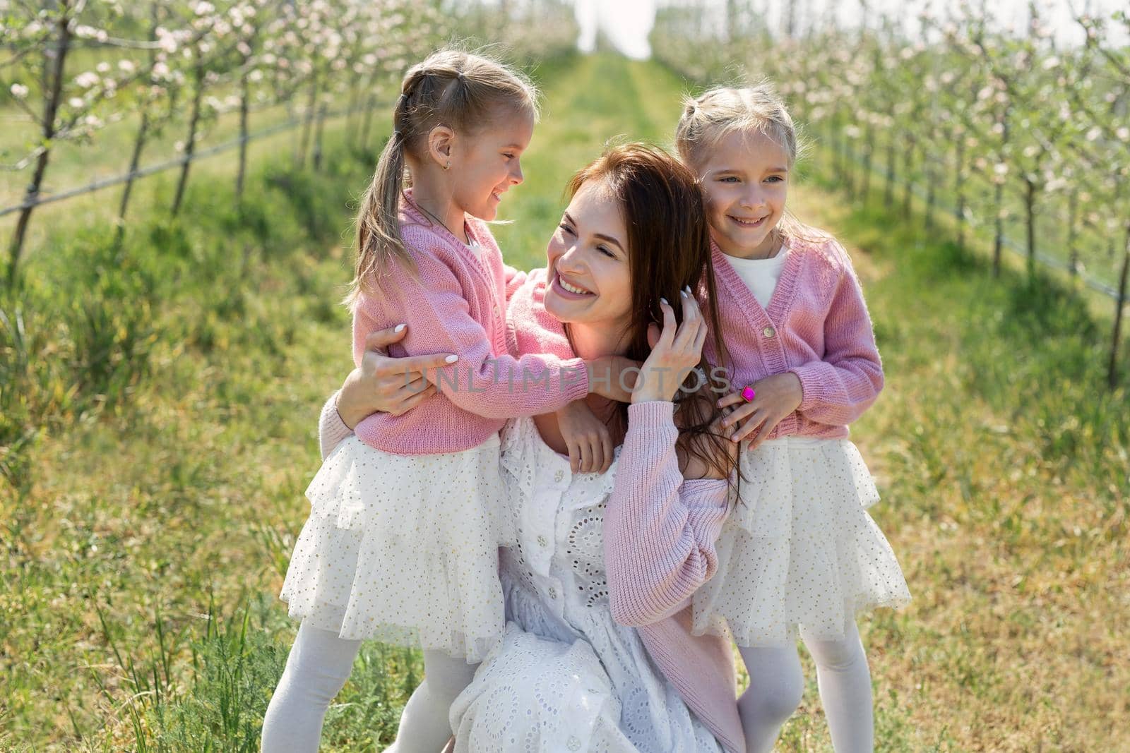 Portrait of a mother and her twin daughters in a blooming Apple orchard.