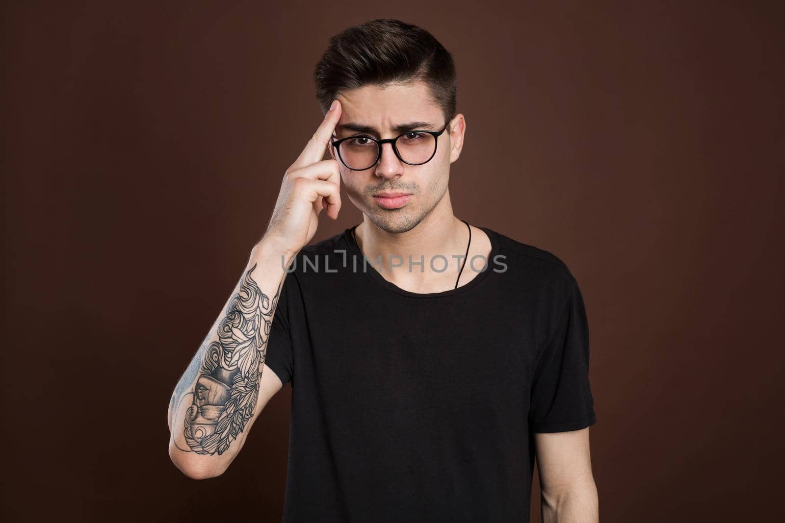Headshot of serious thoughtful middle aged man tries to remember something in his mind, keeps fore finger on temple, keeps eyes shut, isolated over brown background, wears fashionable clothing. by StudioPeace