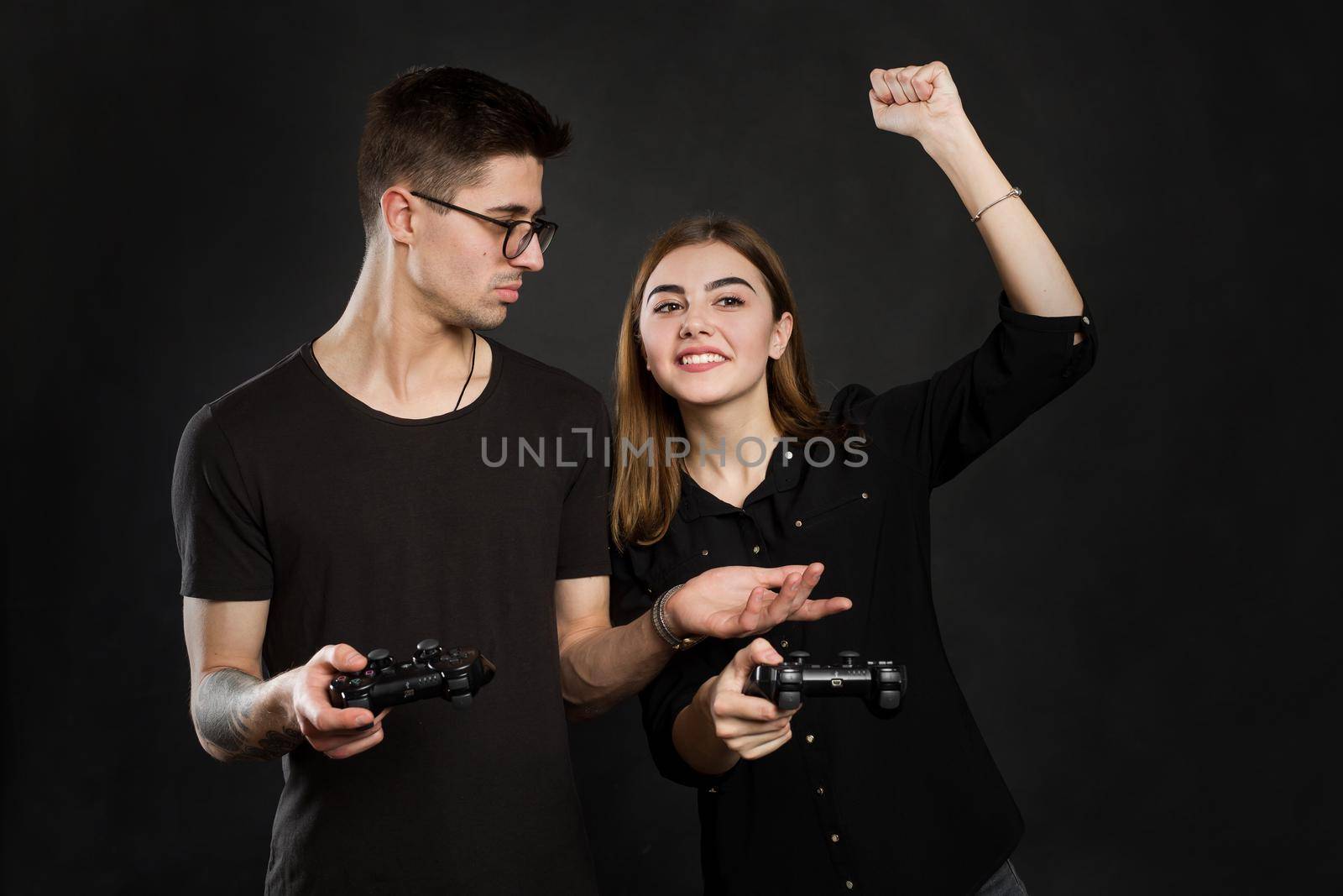Beautiful young couple playing video games with joysticks together, isolated on black background.