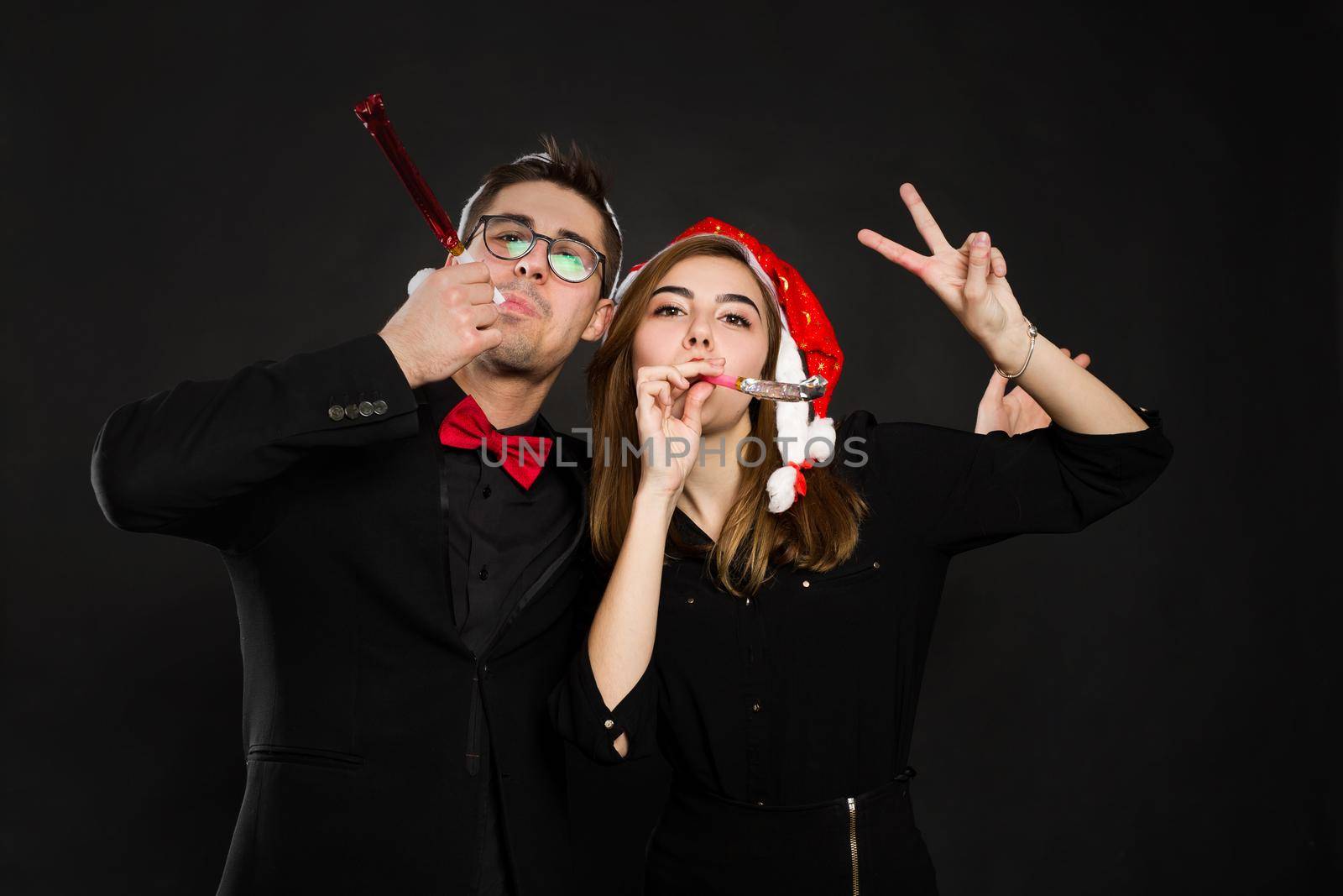 Young couple in love enjoy a new year's party, put on Santa hats and hold pipes in their hands and show the peace sign.