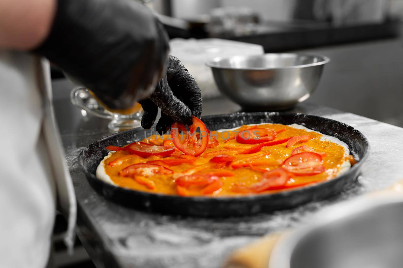 Cooking pizza. Close-up of the chef's hand spreading slices of tomato on the dough.