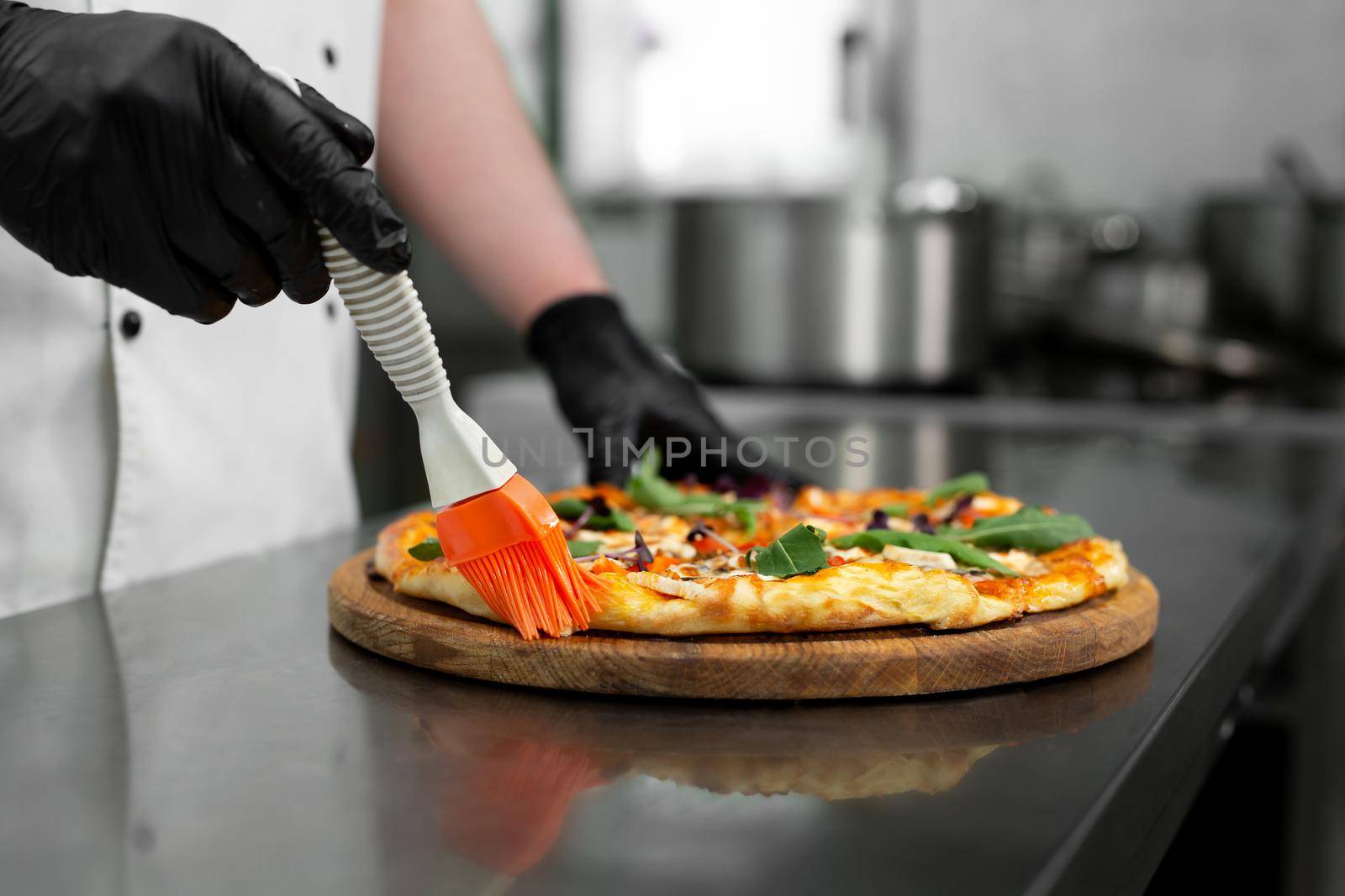 Close-up of the chef's gloved hands smearing the edges of the pizza with oil with a brush.