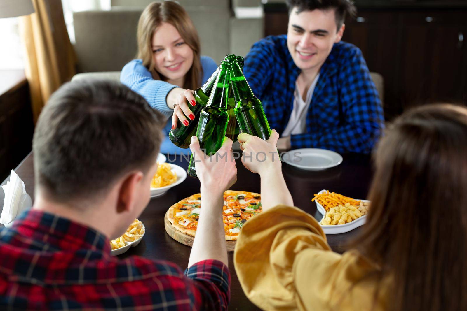 Group of young friends with pizza and bottles of beer celebrate in a cafe by StudioPeace