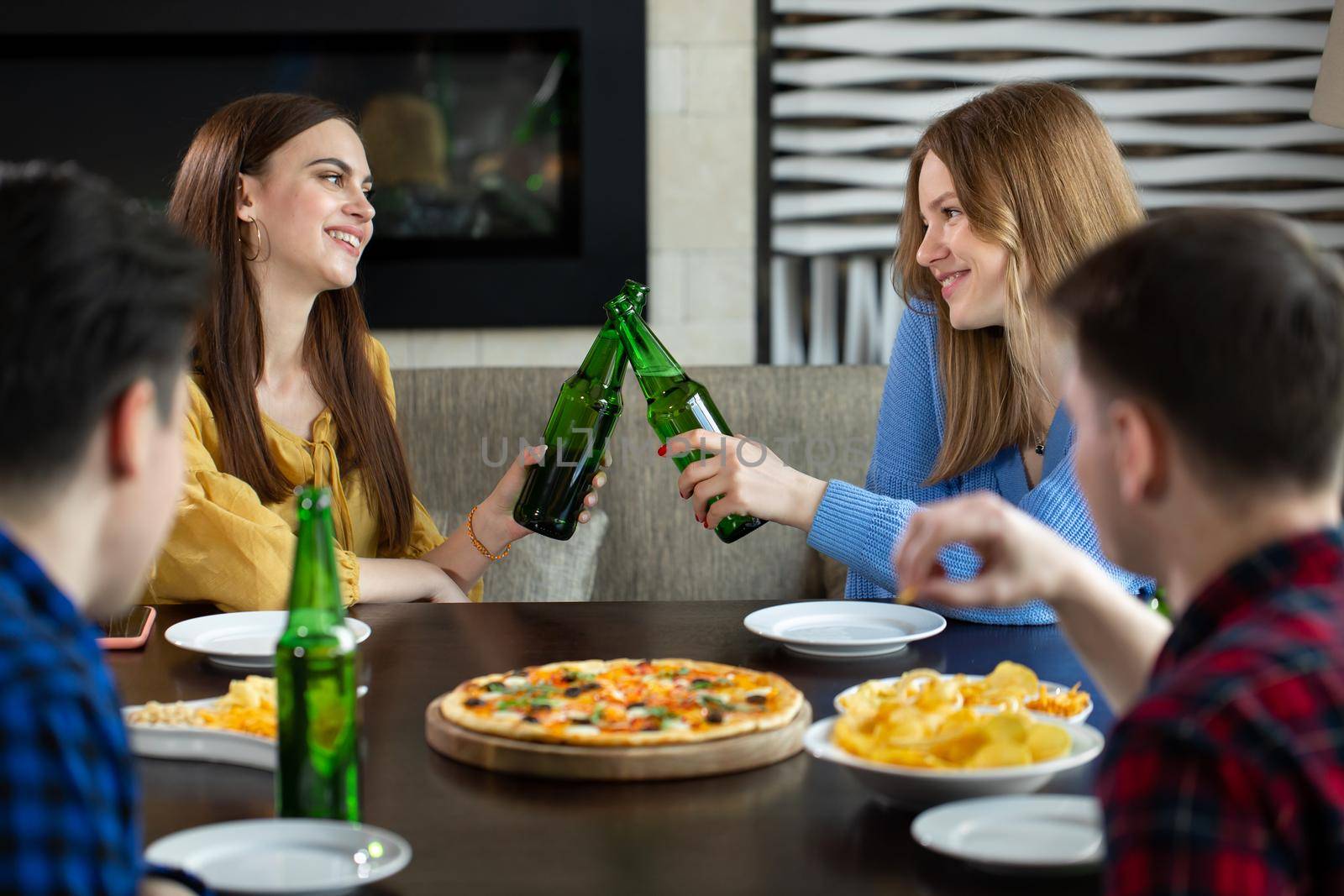 Friends having a drinks in a bar, They are sitting at a wooden table with beers and pizza by StudioPeace