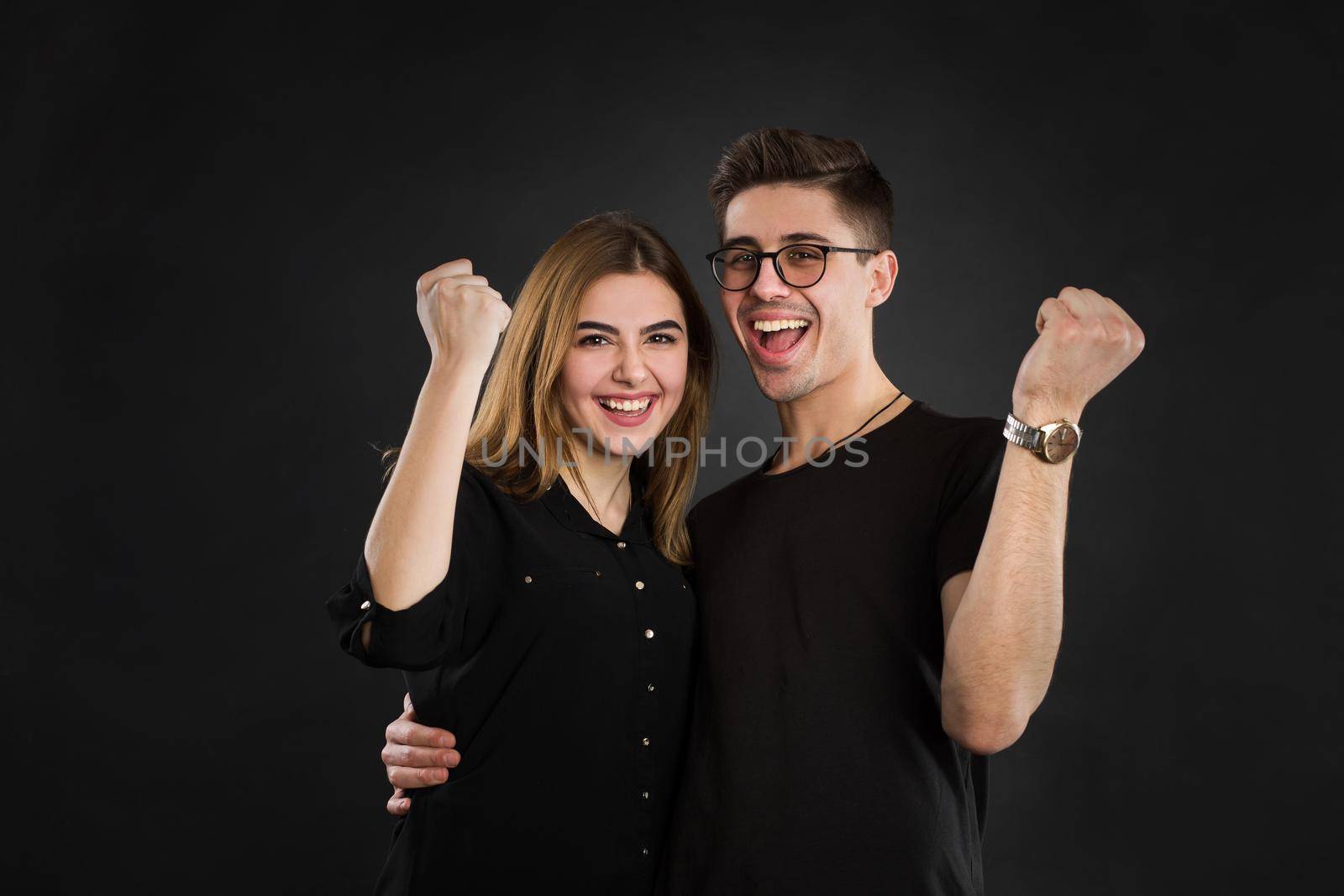 Yes We did it Cheerful couple is celebrating with raised hands, standing on black background in shirt People, happiness, winning, victory, success and good luck by StudioPeace