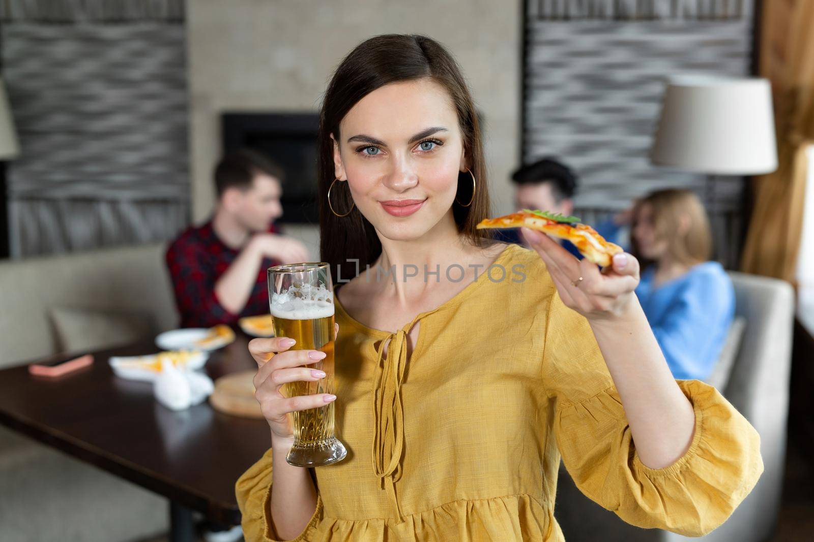 Portrait of a young woman holding pizza and beer in a pub