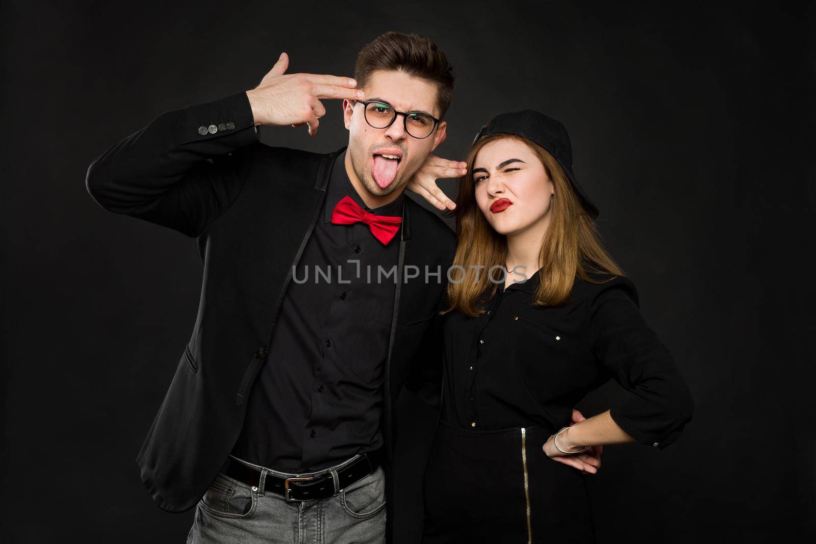 Teenage smiling rap couple in black clothing and a black cap show signs with their hands and tongue. Isolated colors on a black background by StudioPeace