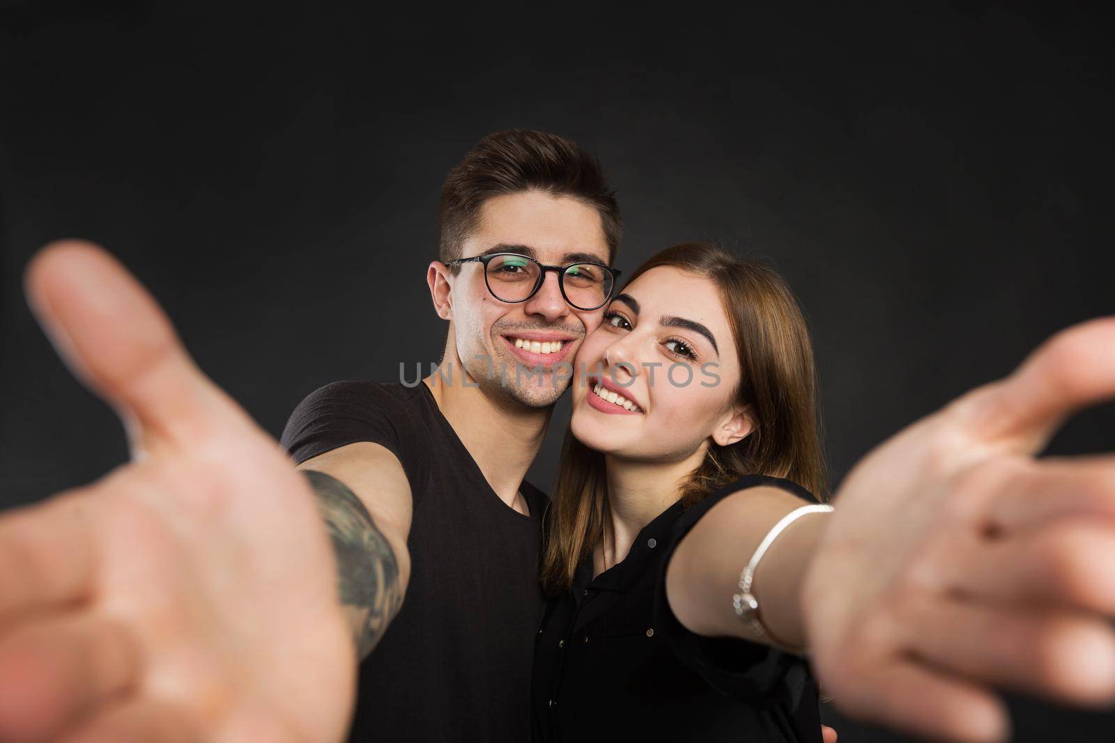 Happy young loving couple making selfie and smiling while standing against black background. by StudioPeace