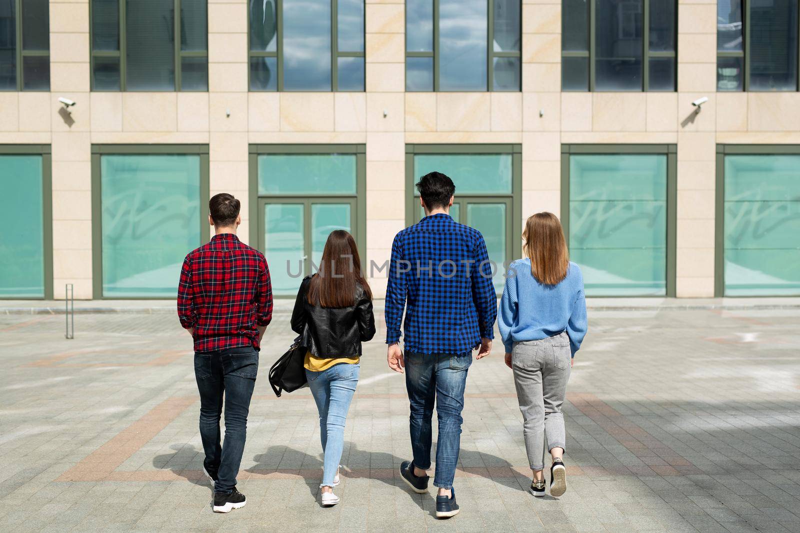 Back view of four friends walking arm in arm down an urban street. by StudioPeace