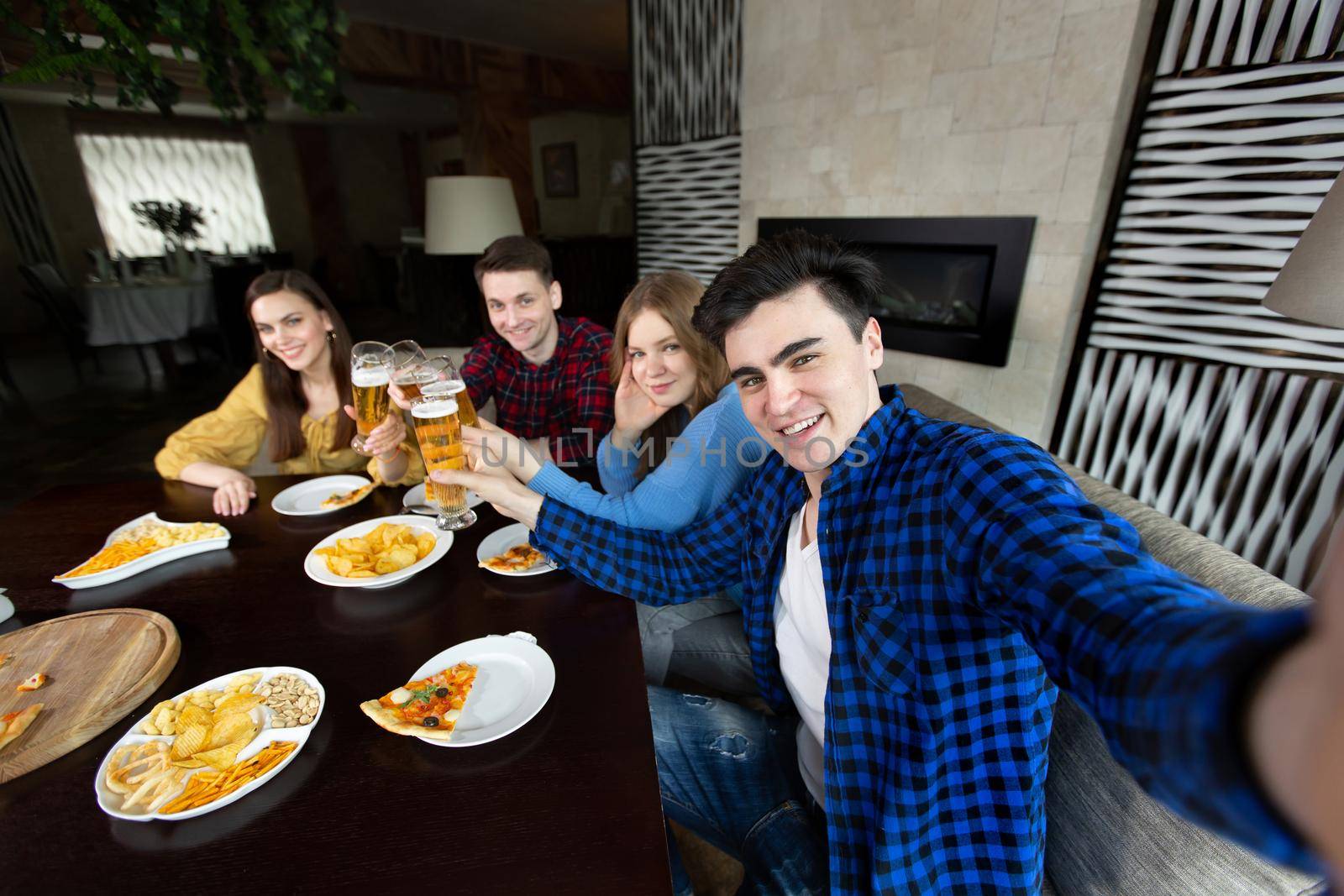 Beautiful young people in casual clothes are resting with pizza and bottles of drink. One guy is making a selfie with his friends. by StudioPeace