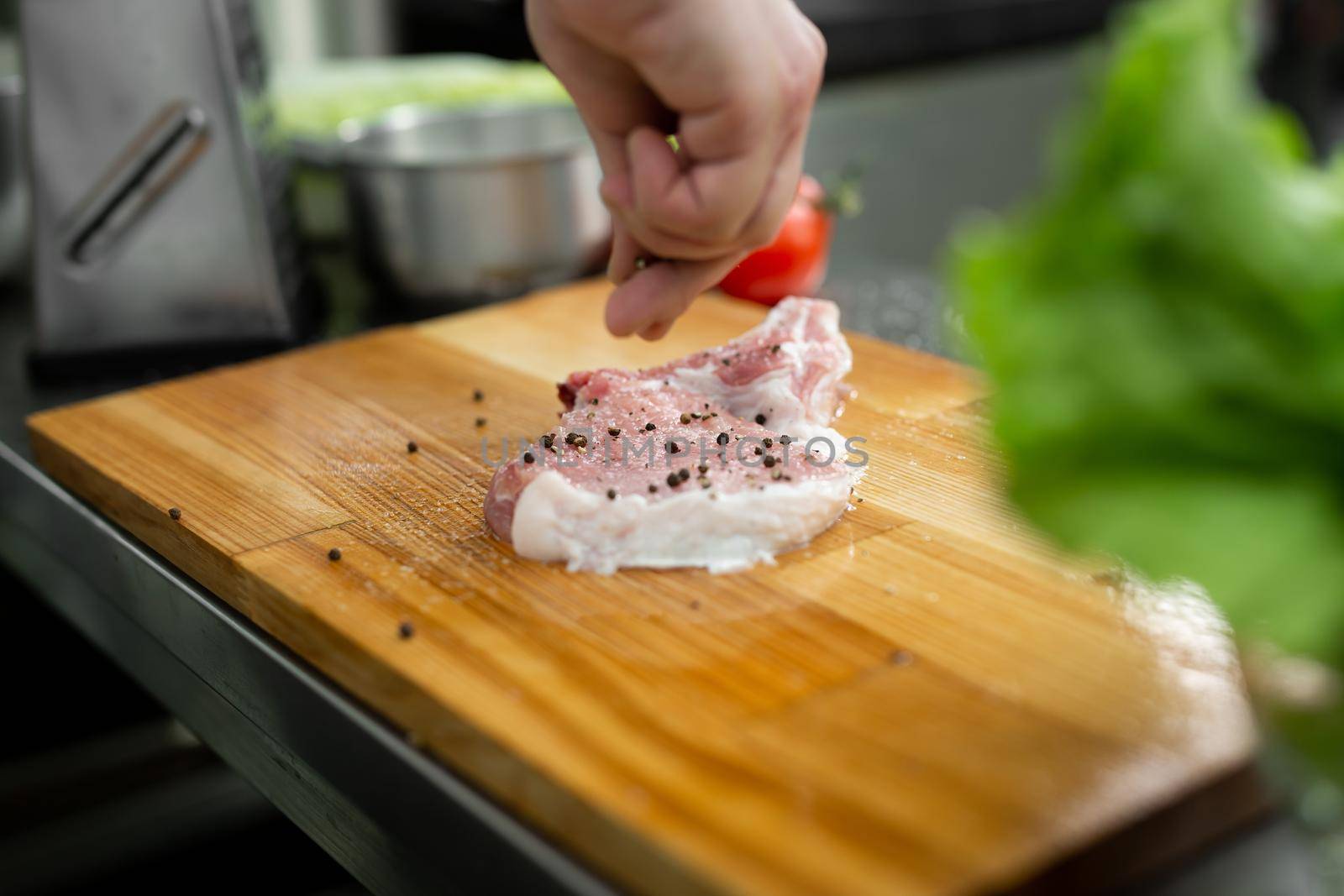 Chef peppering raw beef steak. Professional cook seasoning juicy meat with pepper, salt and herbs before grill. by StudioPeace