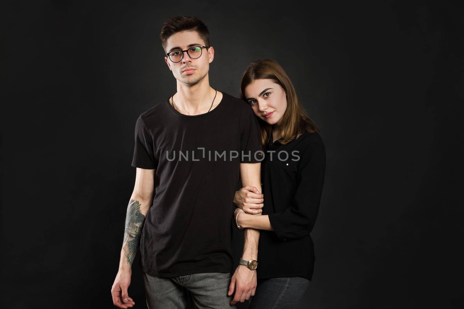 Portrait of young couple in black clothes wearing trendy glasses and posing over black background.