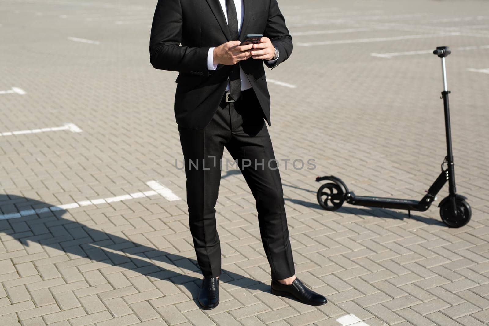 Young handsome businessman in a suit rides an electric scooter and looks at the phone.