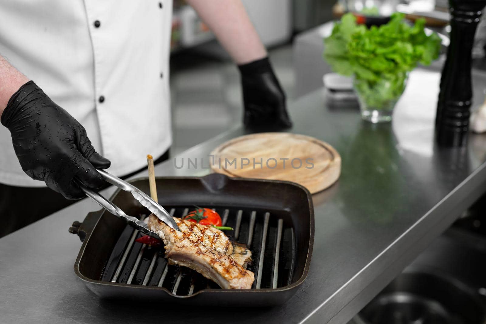 Close-up of a chef's hand holding a grill pan with grilled steaks and vegetables by StudioPeace