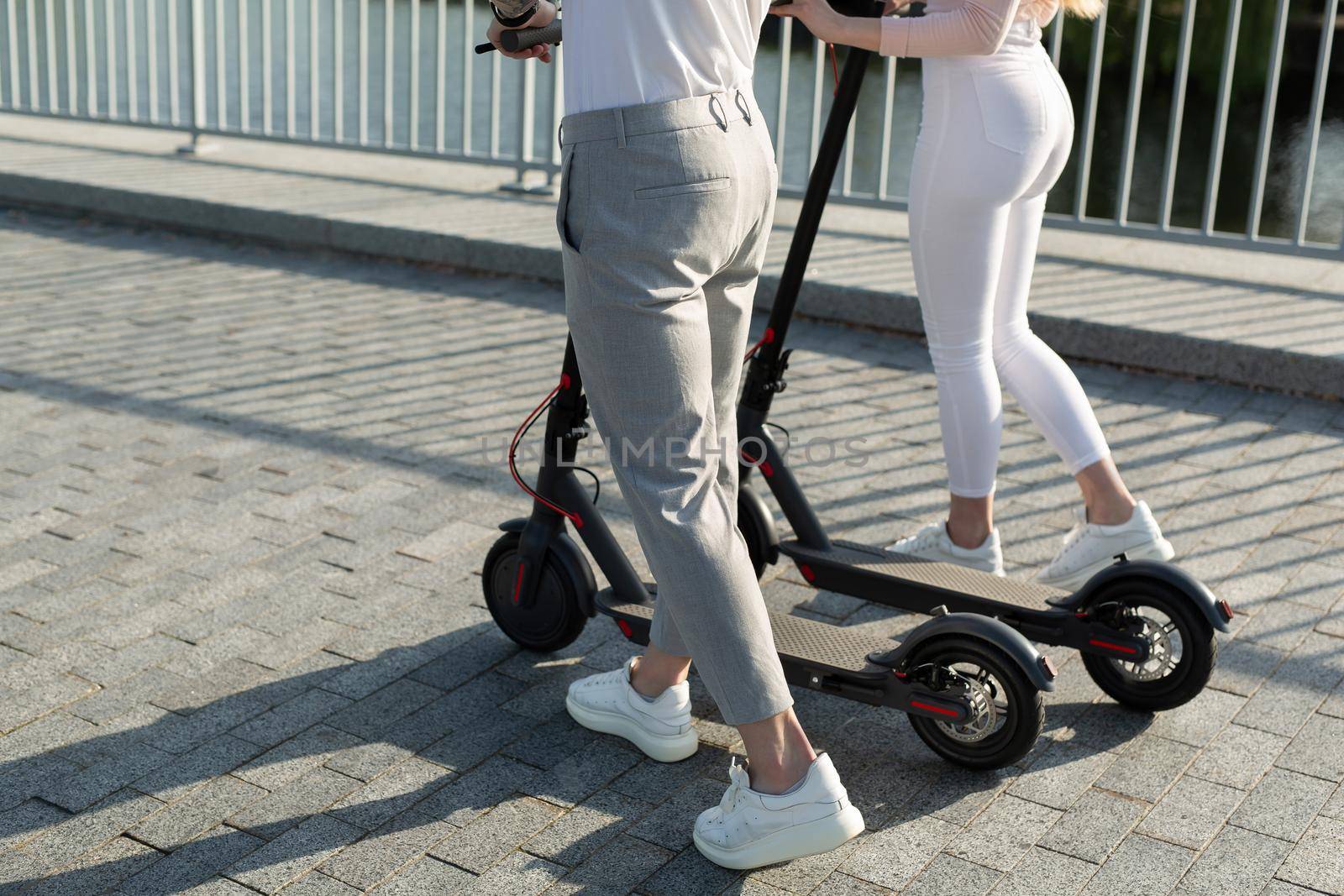 A couple of men and women are walking in the Park and pushing electric scooters by StudioPeace
