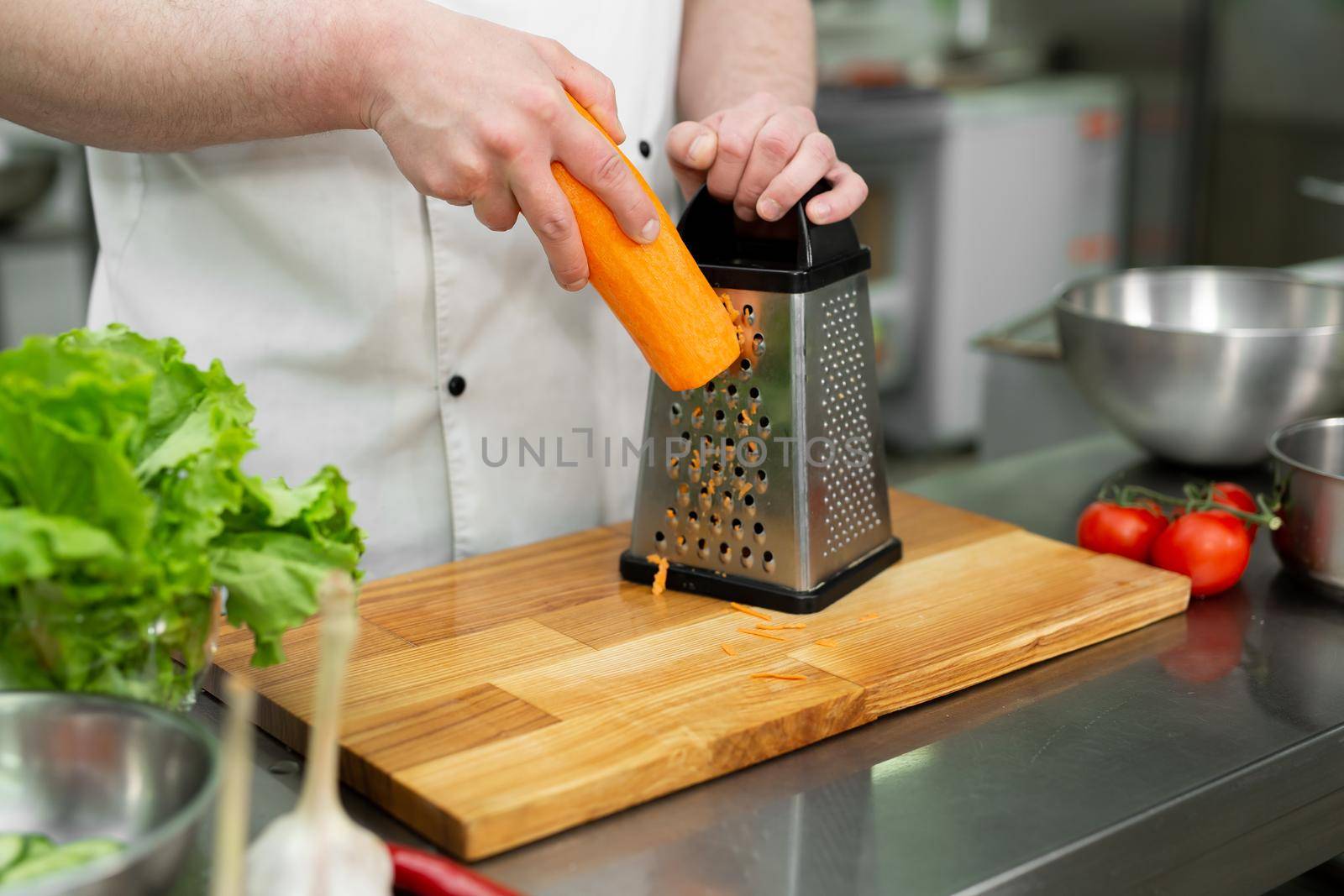 Chef cooks salad by rubbing carrots on a background of vegetables