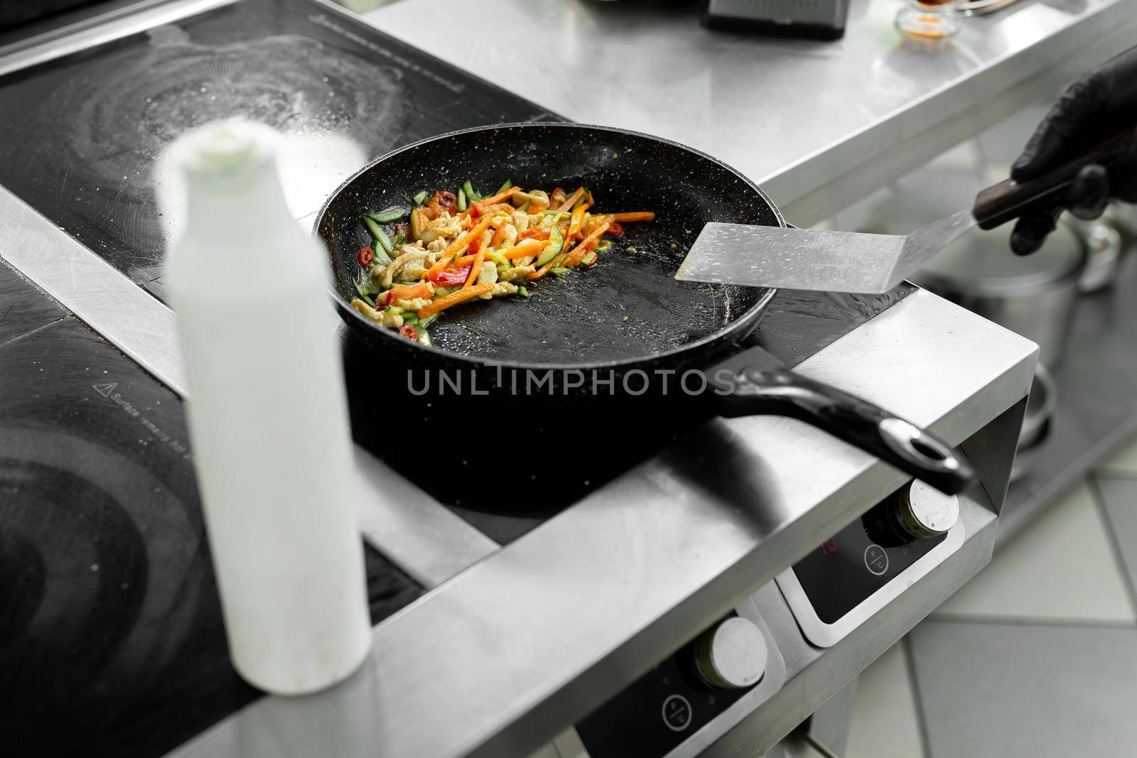 Close-up of the hands of a chef who is frying meat and vegetables in a pan in a restaurant by StudioPeace