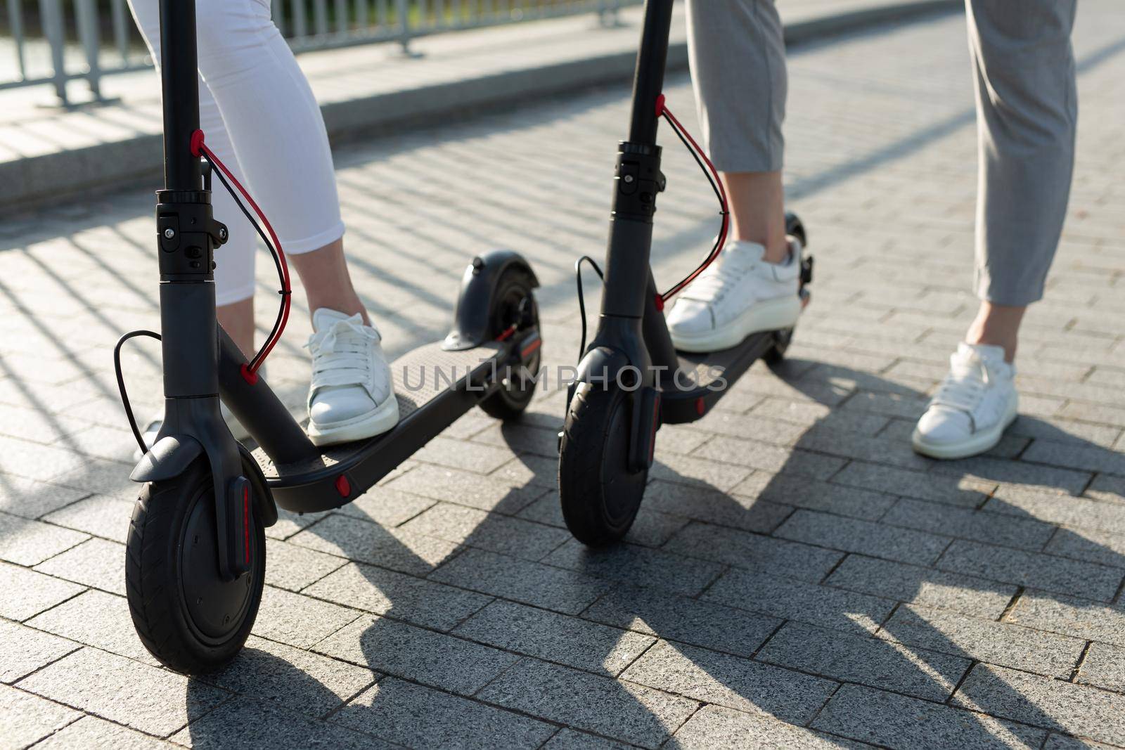 A couple of men and women are walking in the Park and pushing electric scooters by StudioPeace
