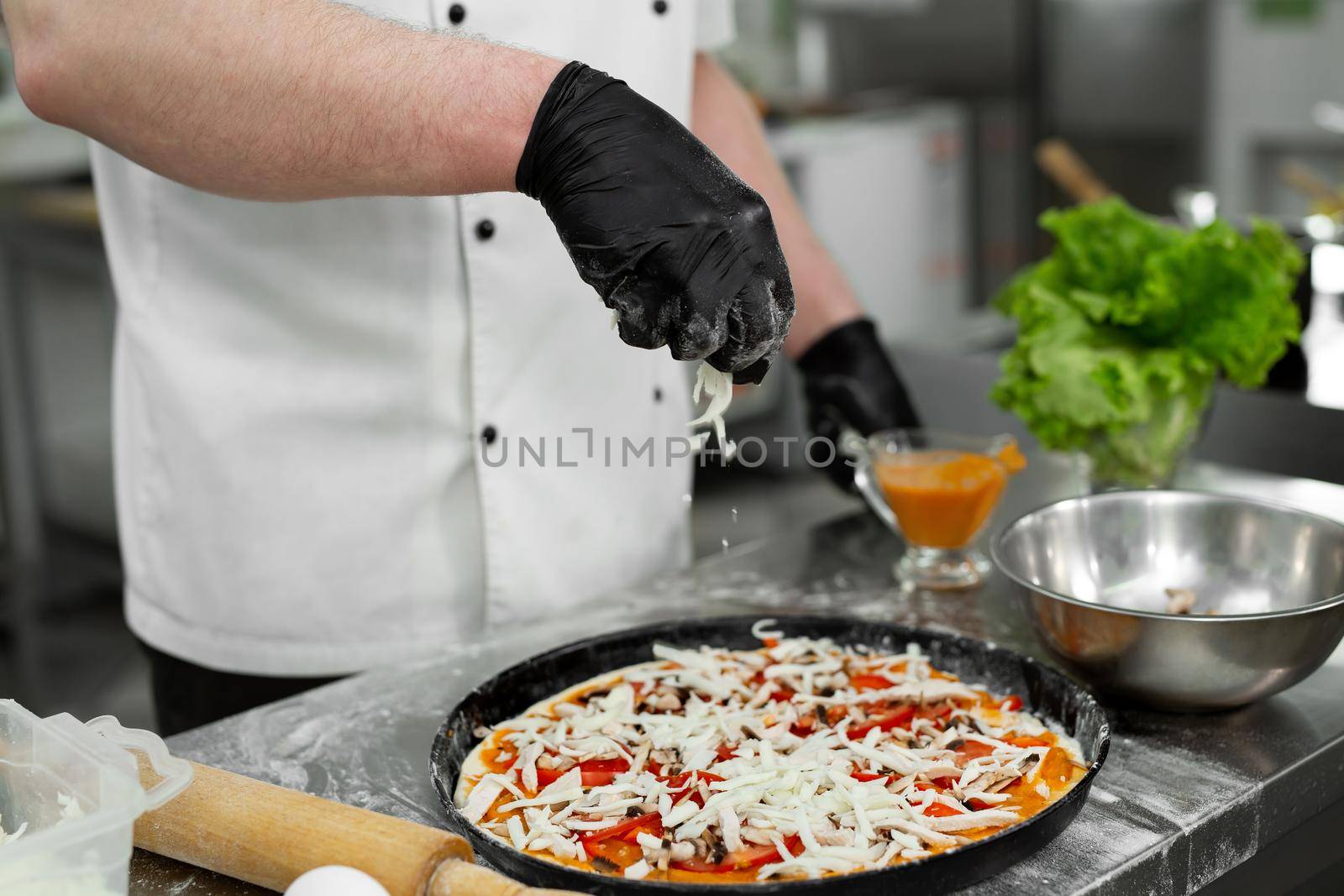 Cooking pizza. Close-up of the chef's hand sipping pizza with grated cheese before baking by StudioPeace