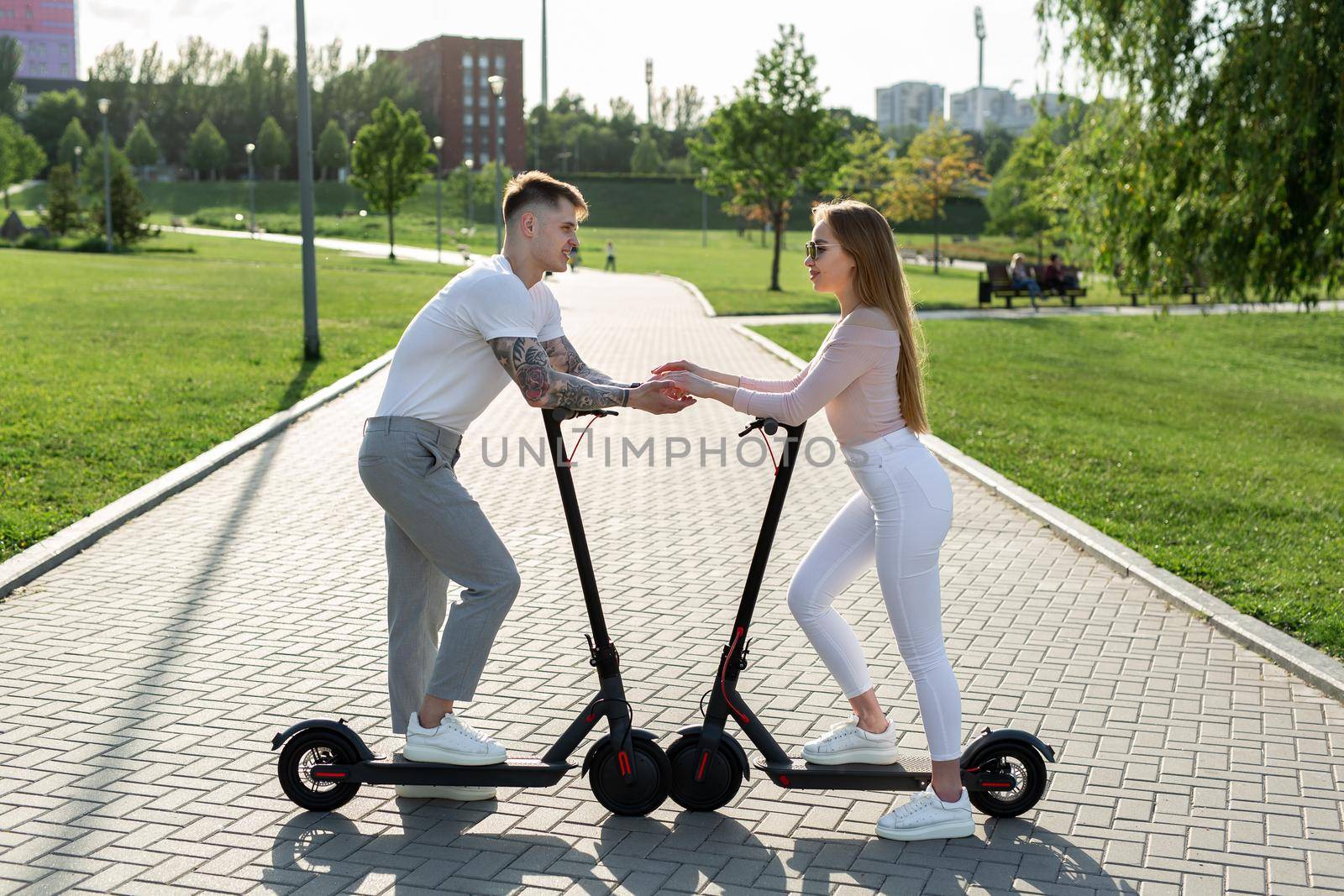Young couple in the park on electric scooters. by StudioPeace